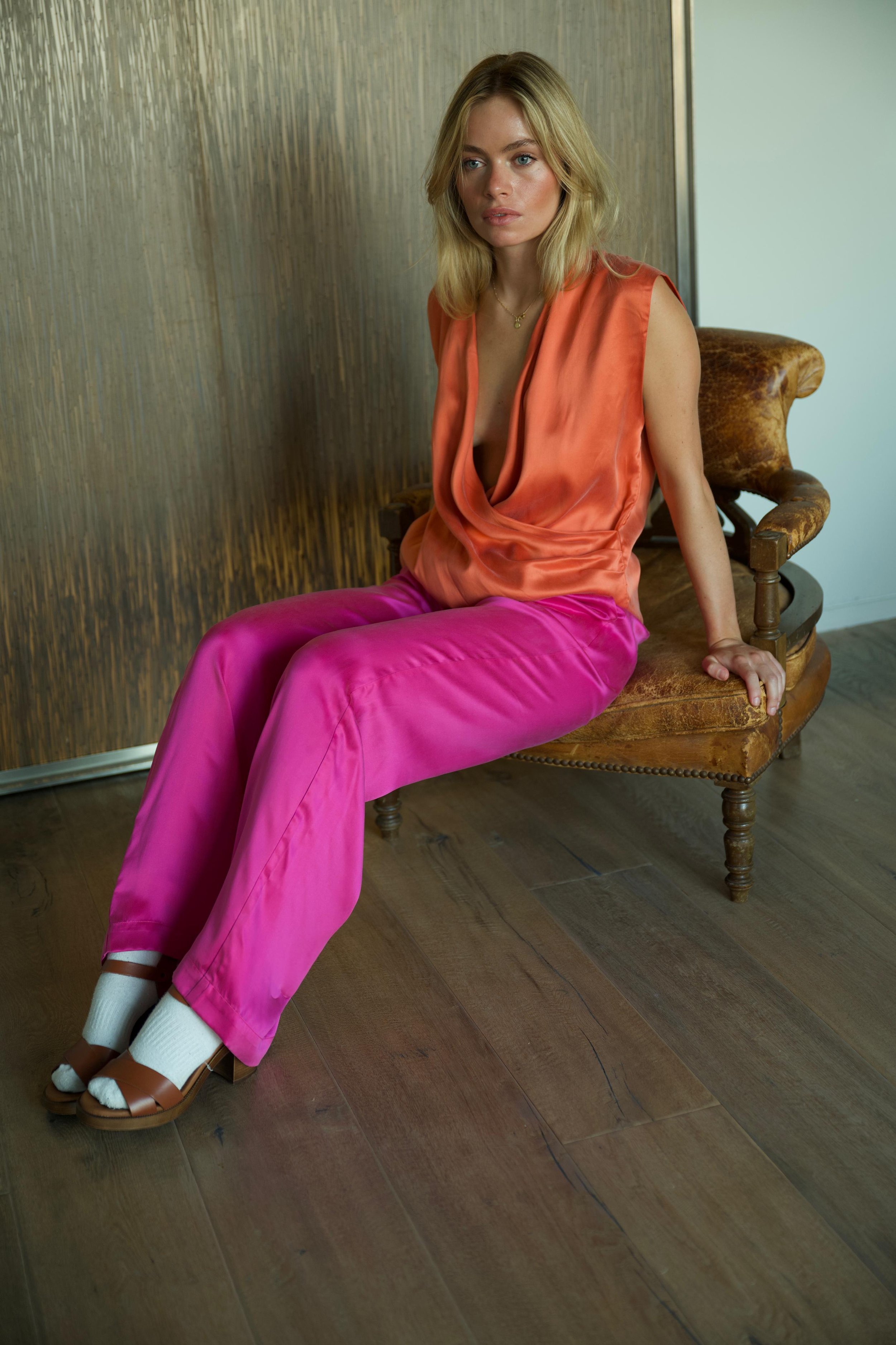Woman wearing orange draped silk top and fuchsia silk trousers, seated