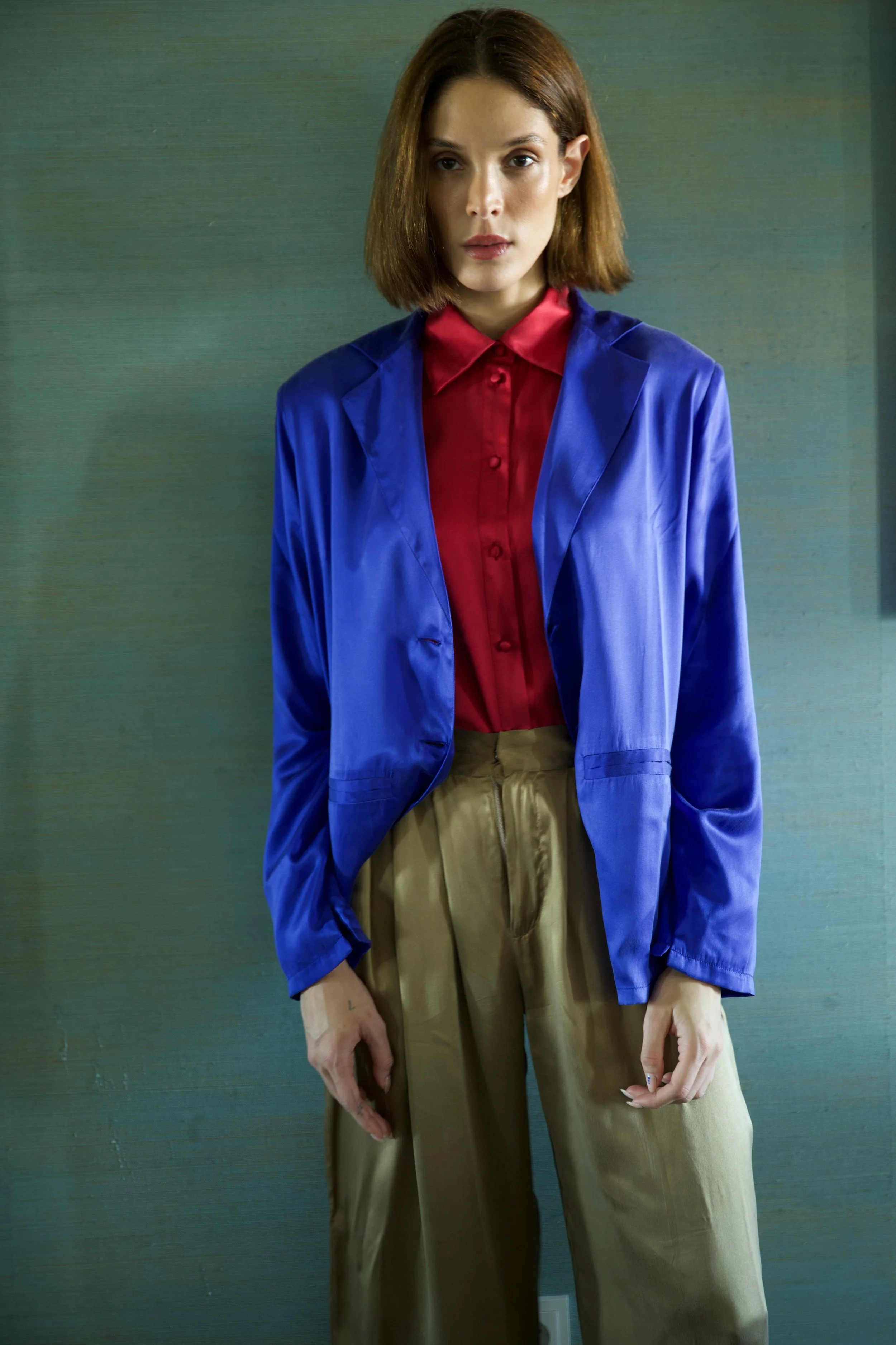 Woman wearing blue silk blazer over red shirt with bronze trousers