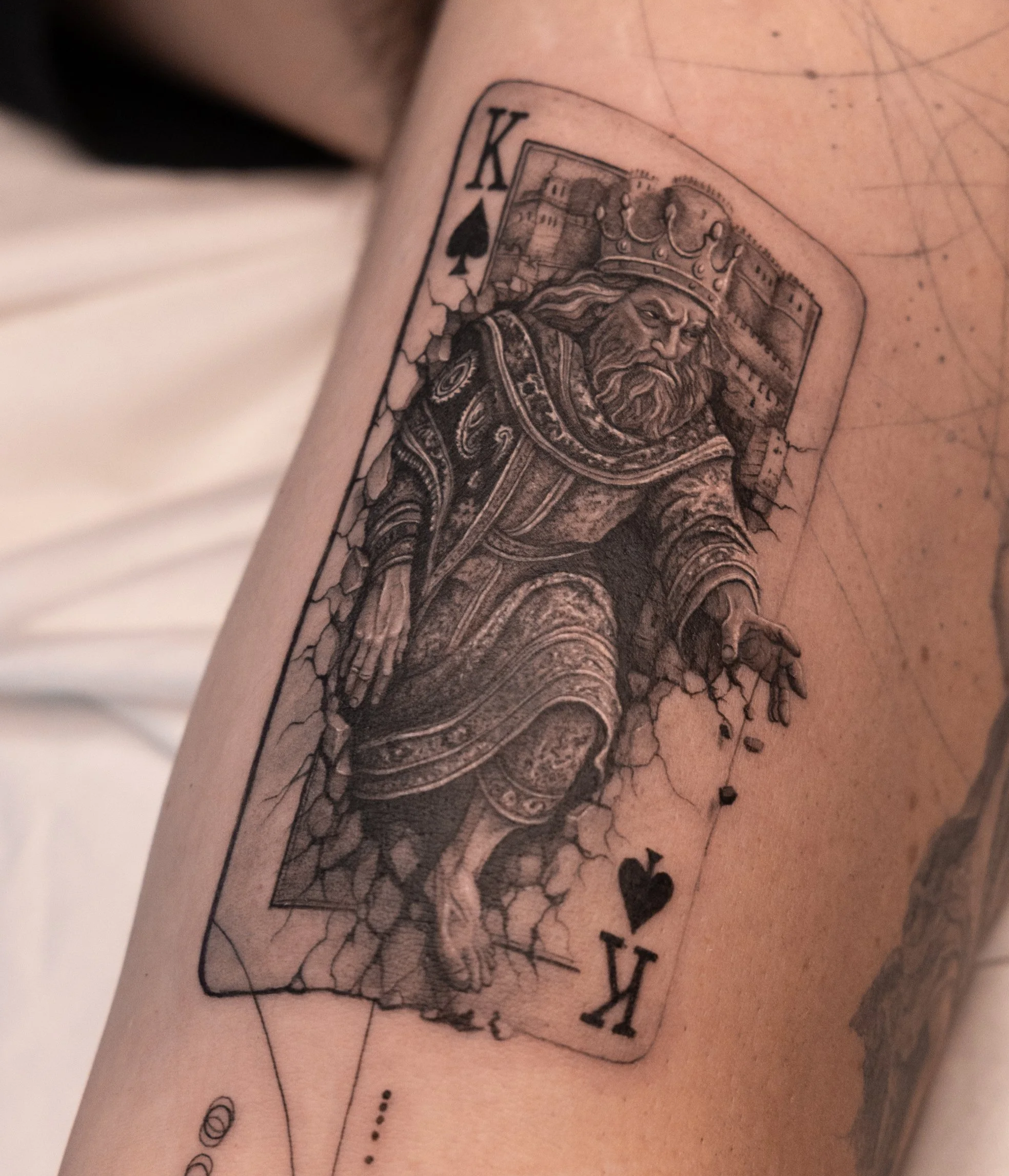 Tattoo of a king of spades playing card with a medieval king illustration, shown on a person's arm.