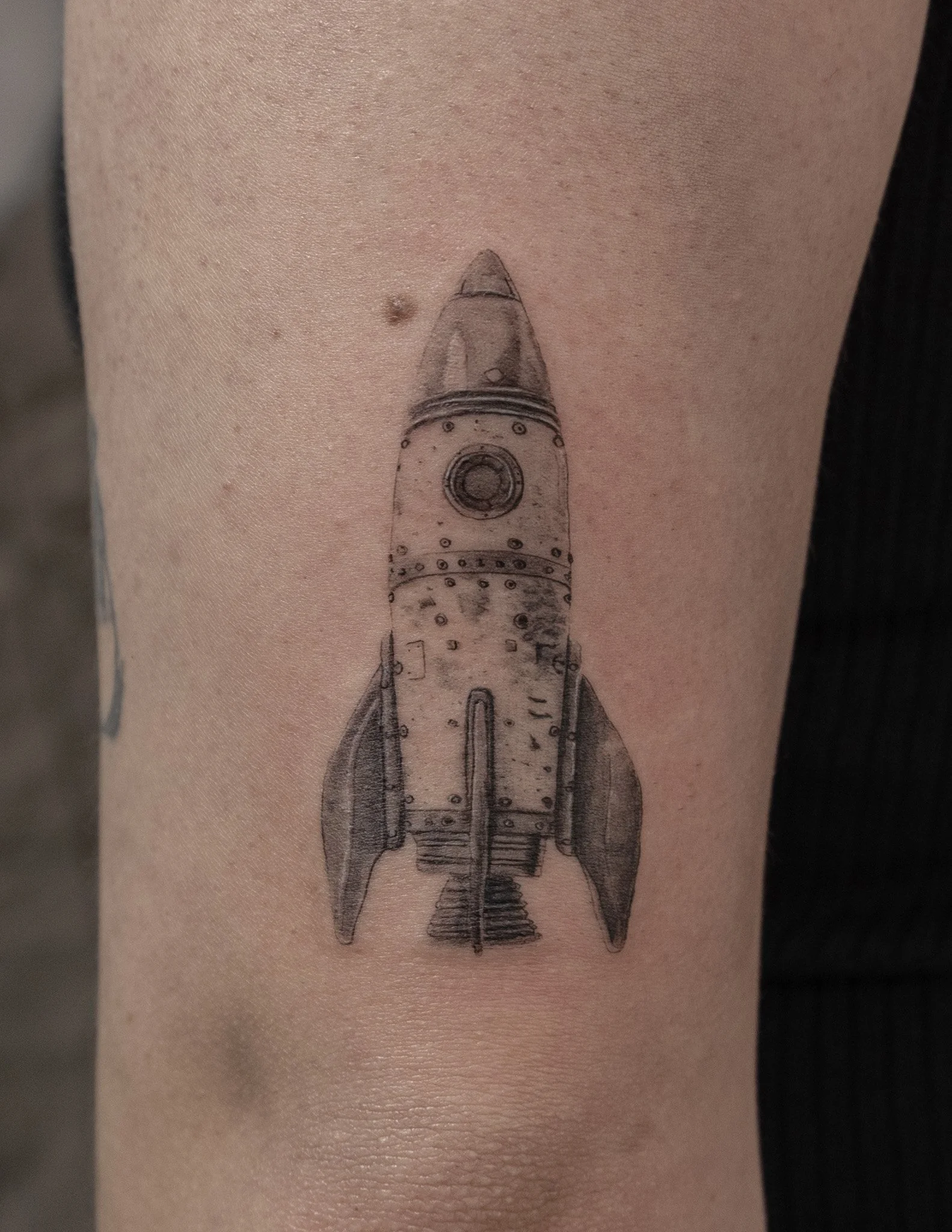 Tattoo of a vintage rocket ship on person's arm