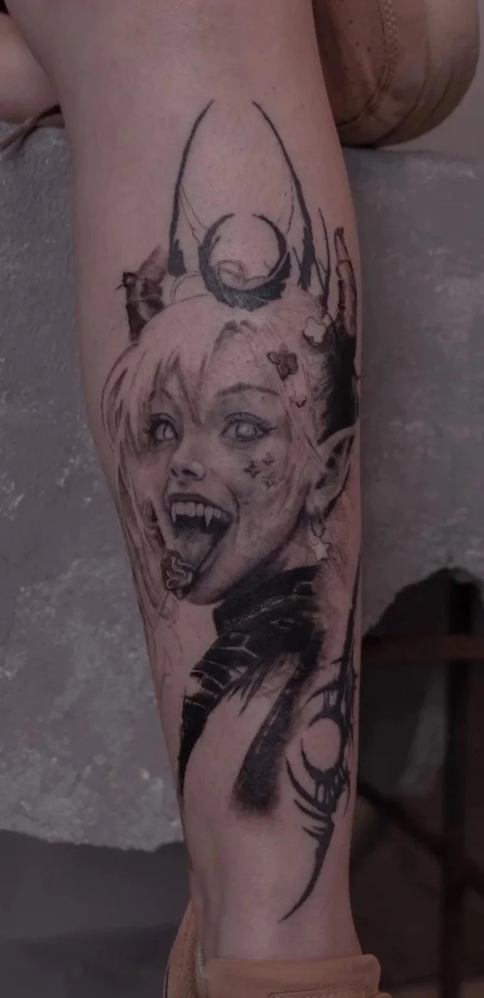Tattoo of a fantasy female character with pointed ears, long tongue, and facial markings, featuring a deer skull with antlers above her head.
