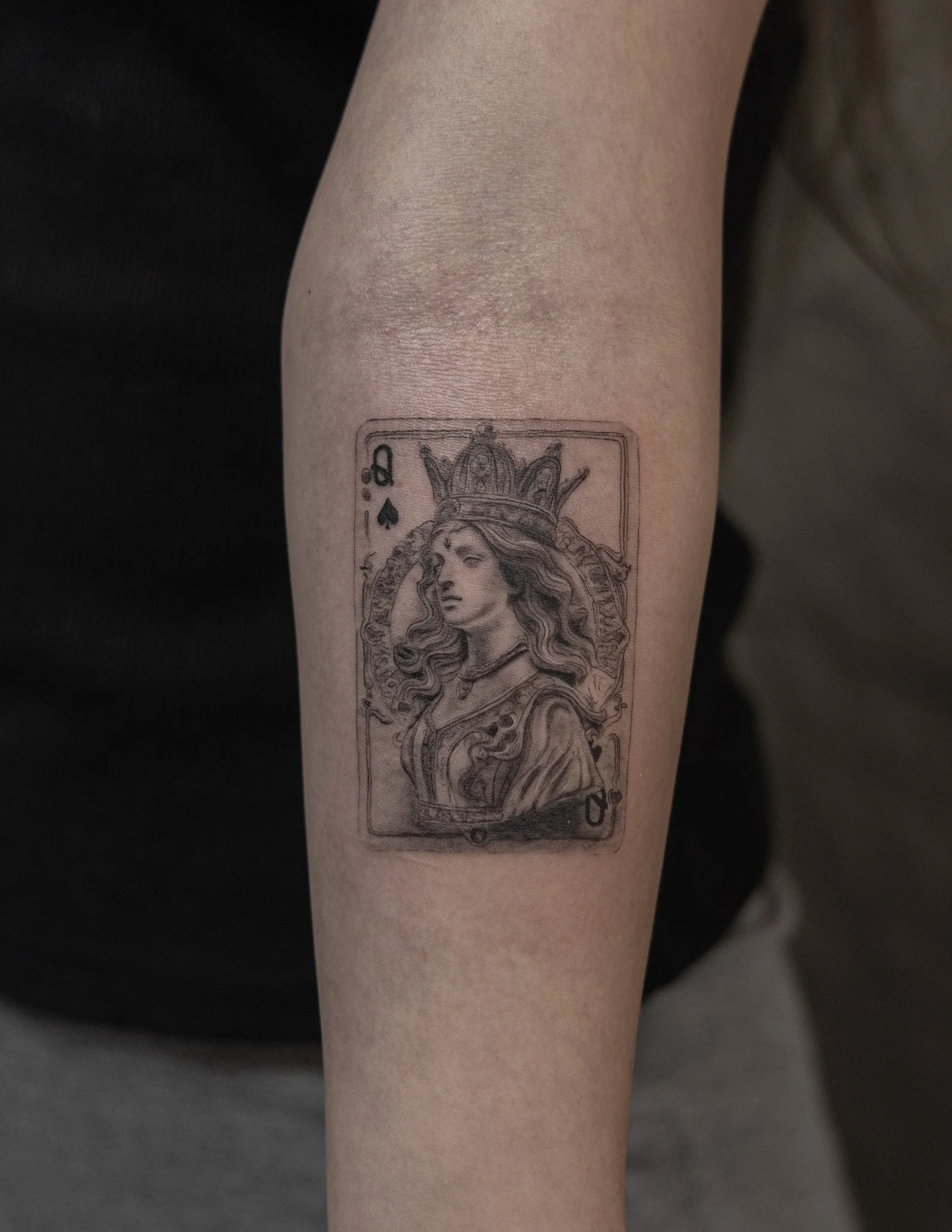 Tattoo of the Queen of Spades playing card featuring a detailed illustration of a regal woman with a crown and flowing hair.