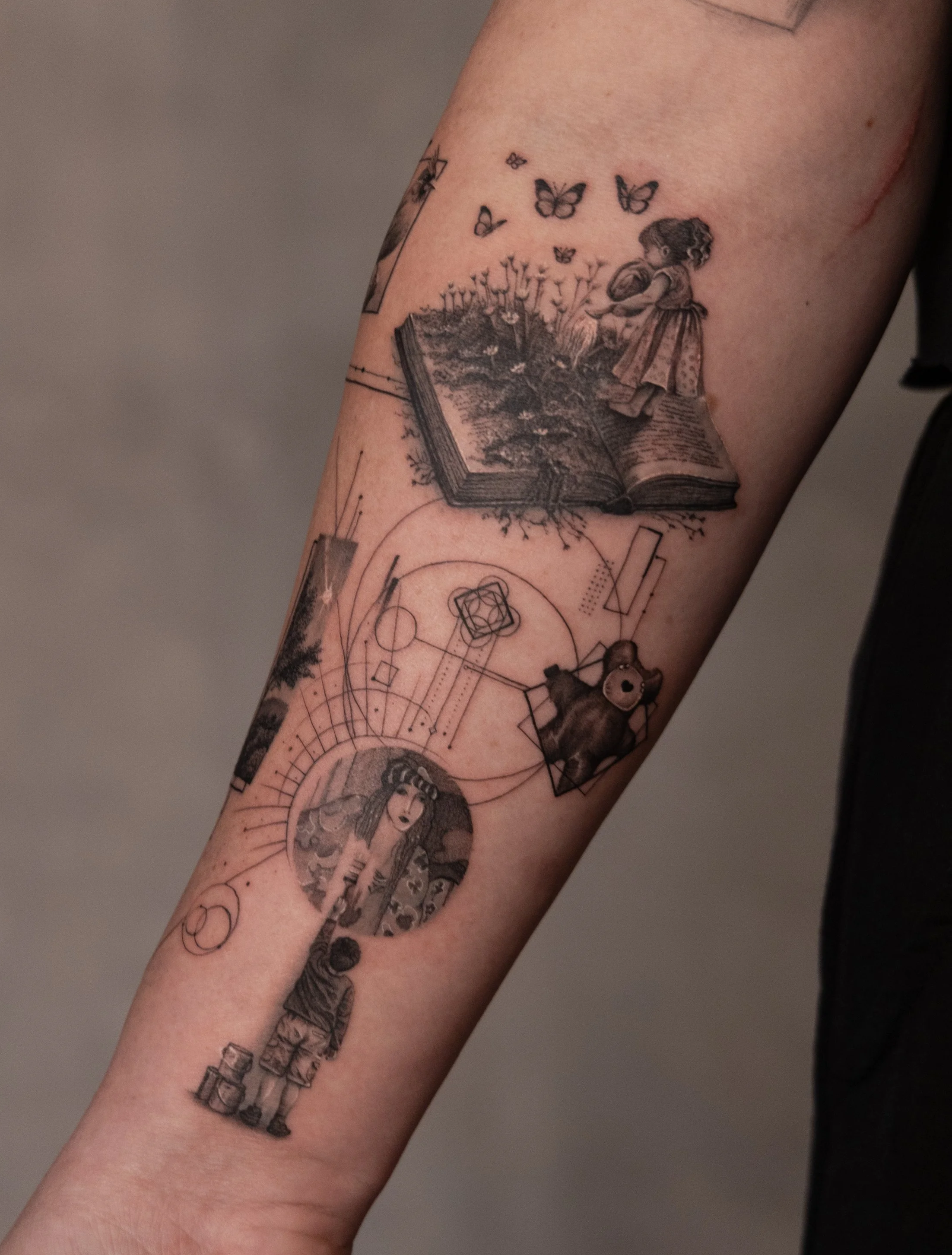 Tattoo of a girl reading a book with butterflies flying above, geometric shapes, a teddy bear, and a woman with long hair holding a paintbrush on the forearm.