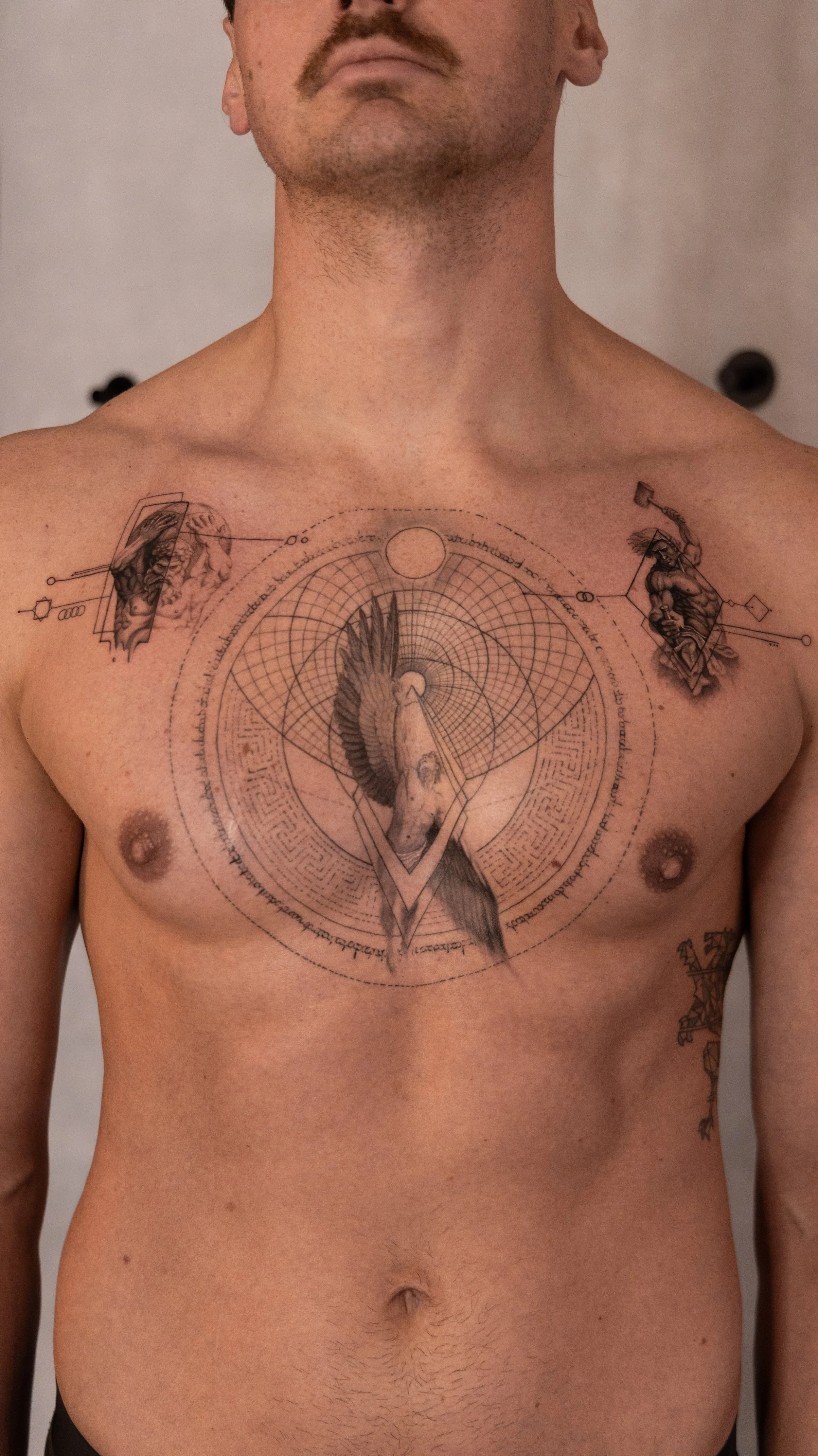 Tattoo of a horse's head, geometric shapes, and circular patterns on a man's chest, with additional smaller tattoos on his shoulders and side.