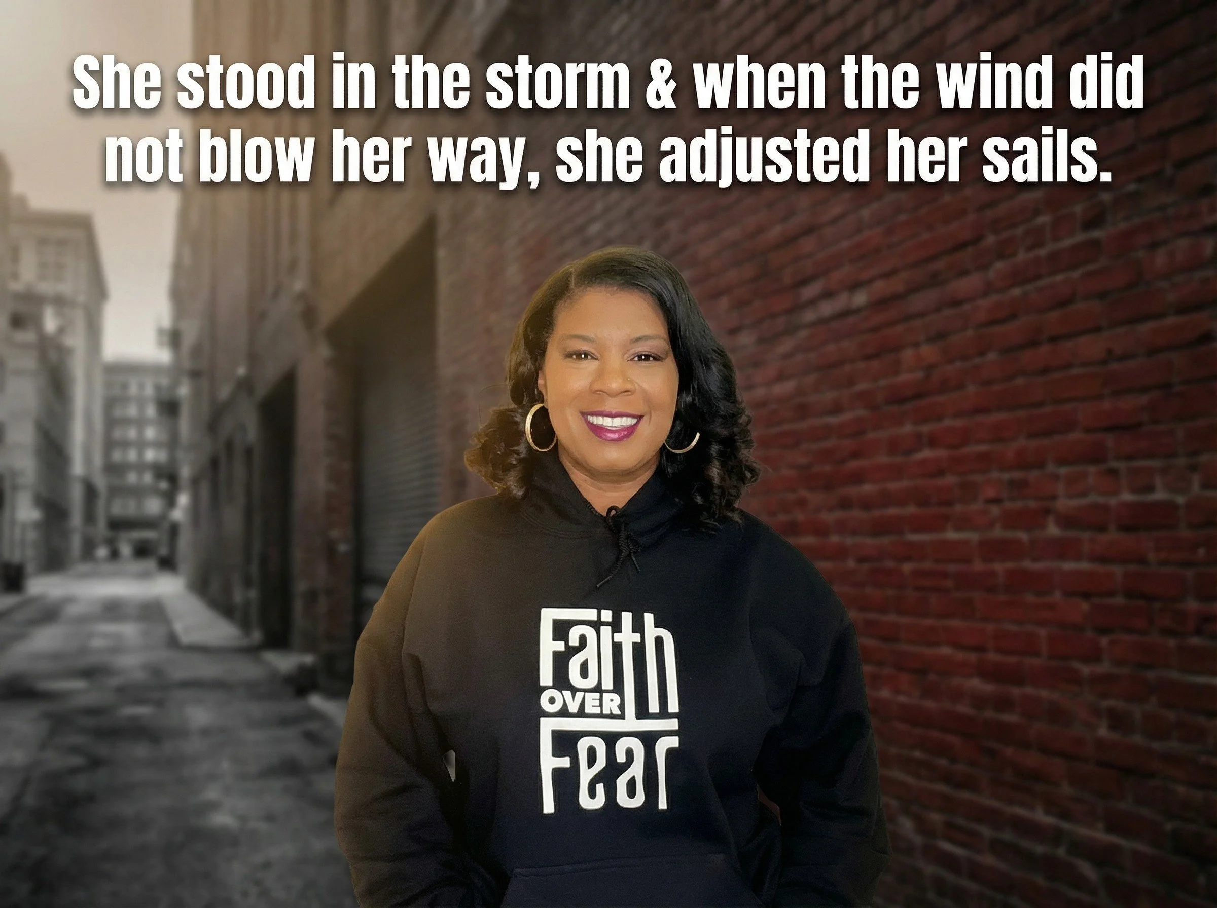 A woman with shoulder-length black curly hair, wearing hoop earrings and a black hoodie with the words "Faith over Fear" printed on it, standing in an alleyway with a brick wall behind her. The image features an overlaid quote saying, "She stood in the storm & when the wind did not blow her way, she adjusted her sails."
