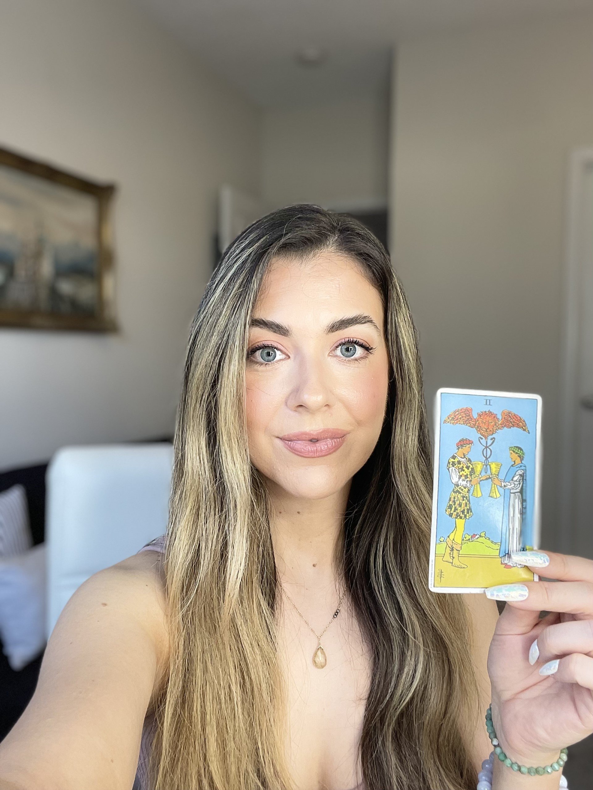 Melissa holding the Two of Cups tarot card while explaining her grounded empowerment-focused reading approach.