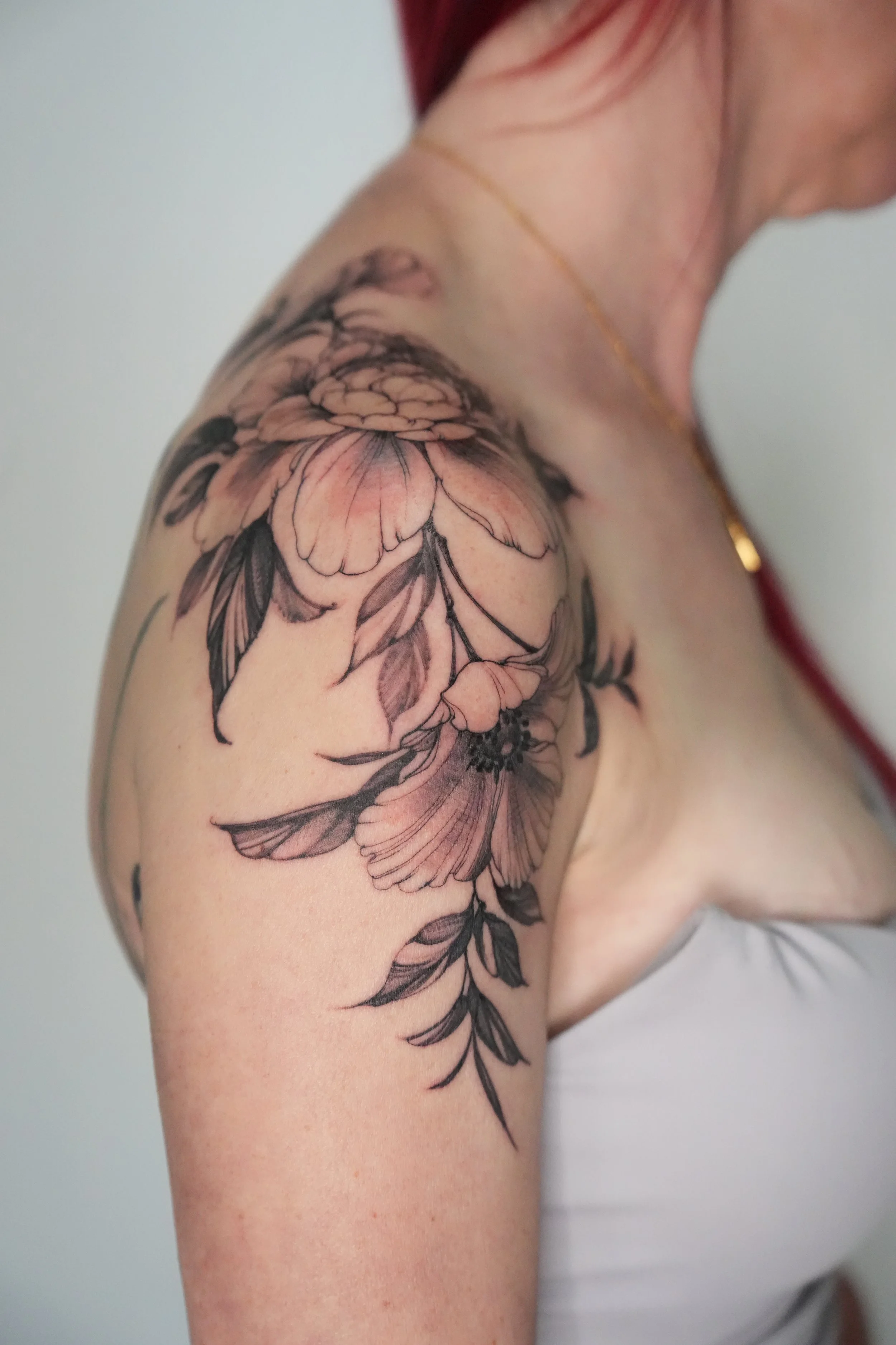 Close-up of a woman's shoulder with a detailed black and gray floral tattoo.