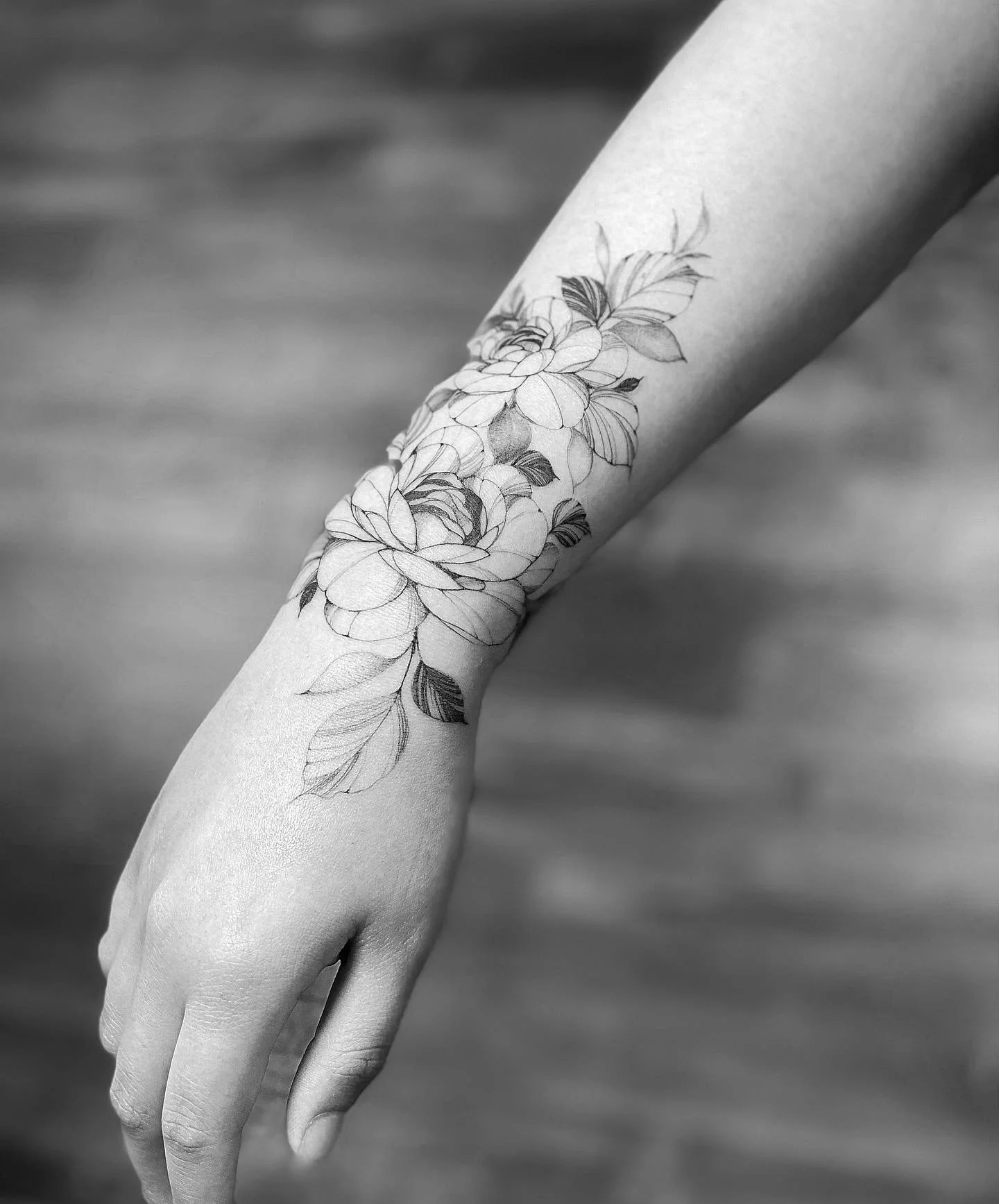 Black and white photograph of a woman's forearm and hand with a floral tattoo design.