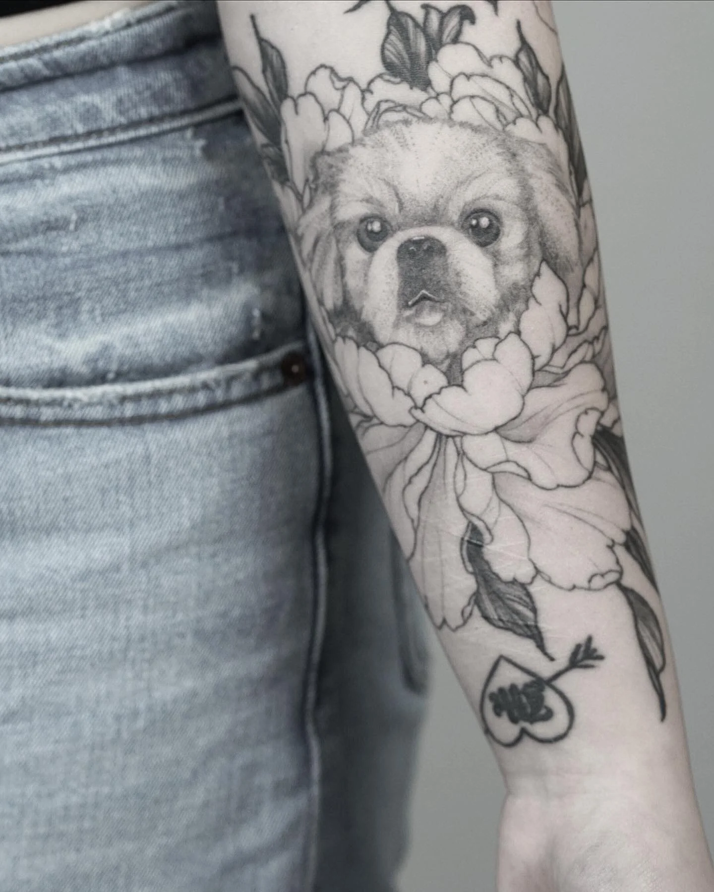 Tattoo of a dog's face surrounded by flowers on a person's arm, with part of denim jeans visible.