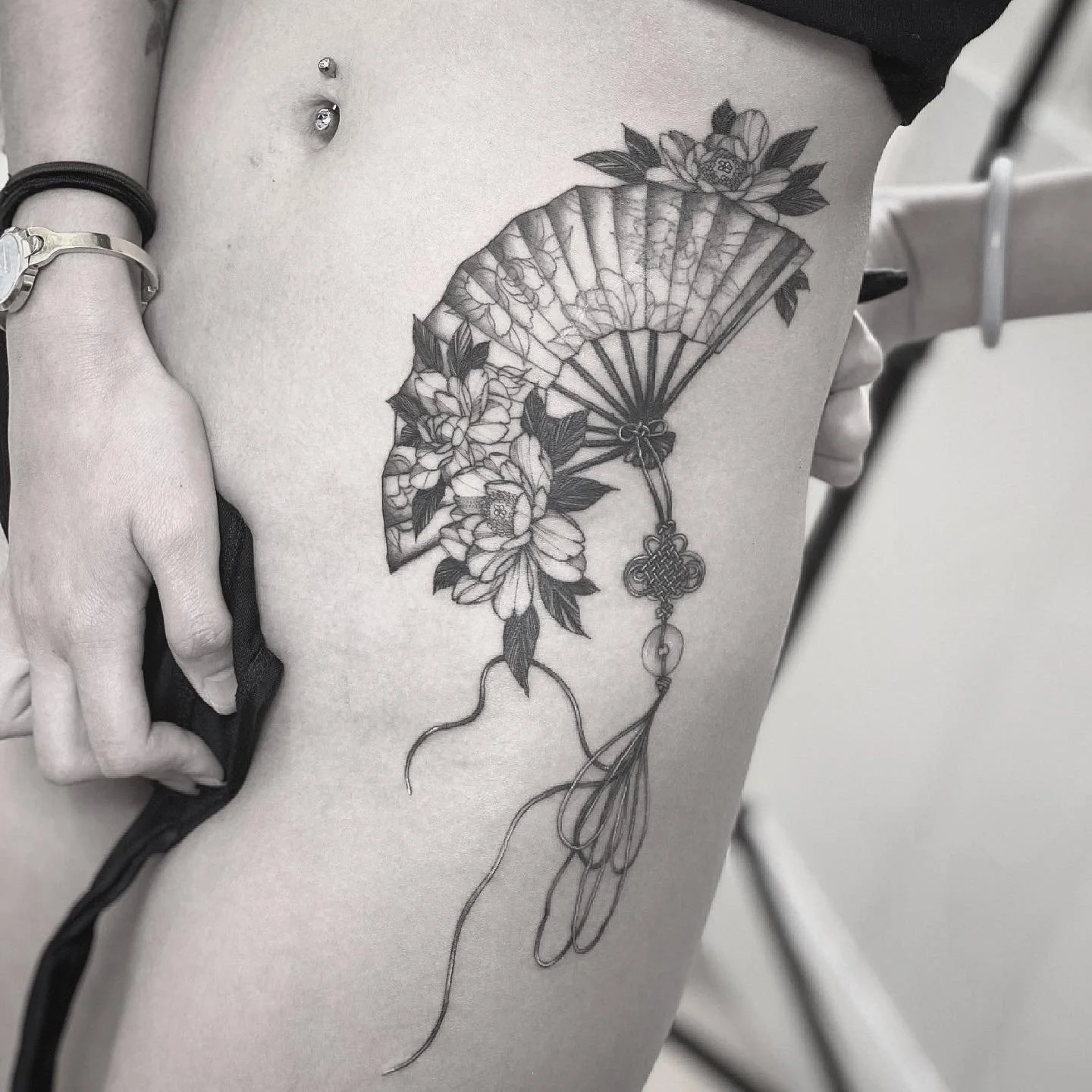 Tattoo of flowers and a folding fan on a person's thigh