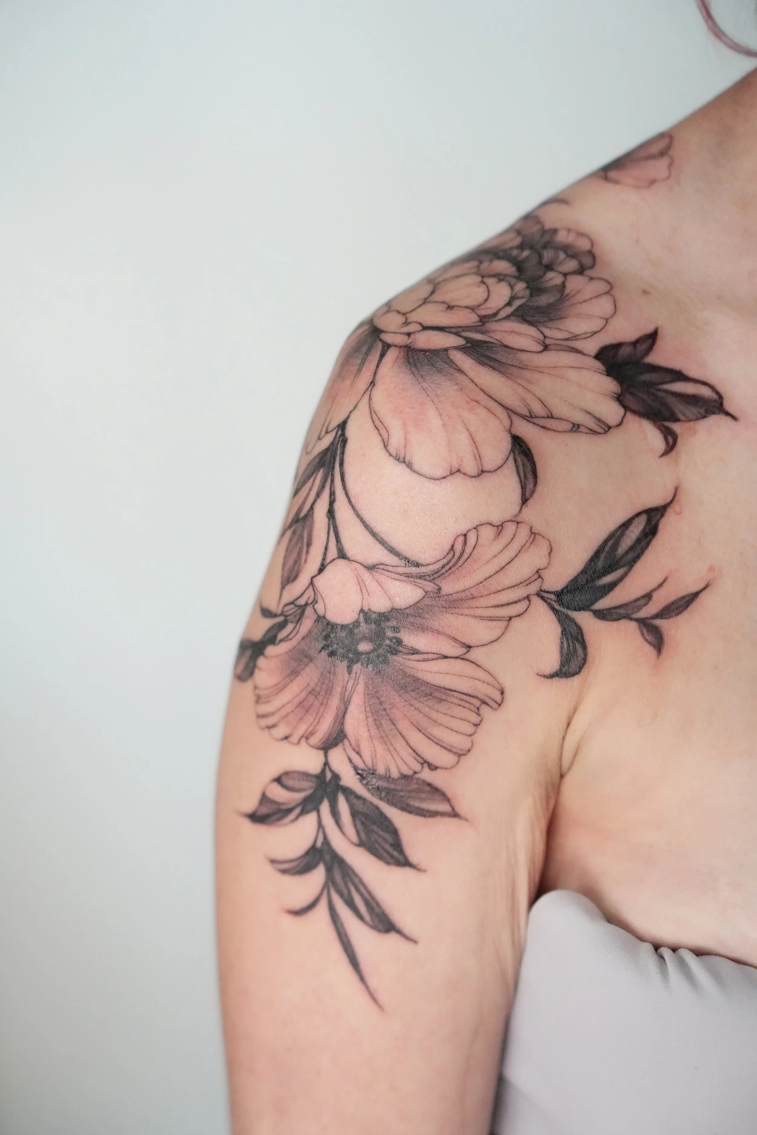 Close-up of a floral tattoo on person's shoulder featuring pink and black ink flowers with leaves.