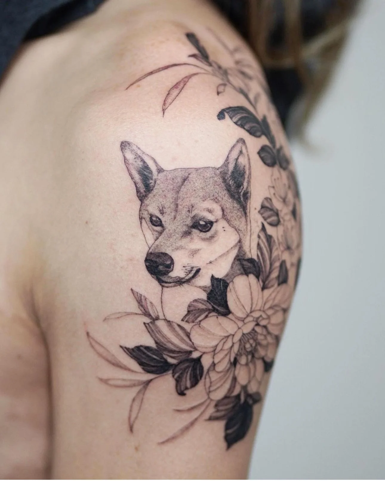 Tattoo of a dog's face surrounded by floral designs on person's shoulder