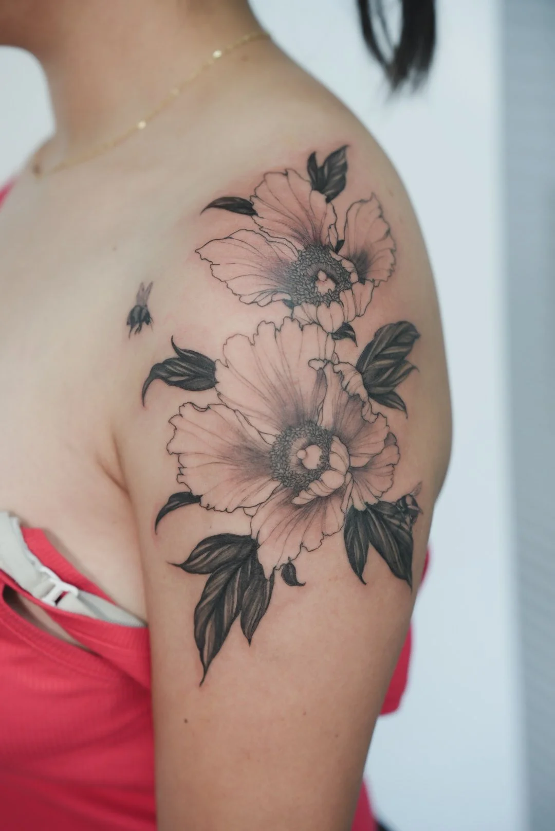 Black and gray floral tattoo featuring two large flowers with detailed petals and leaves on a woman's shoulder and upper arm.