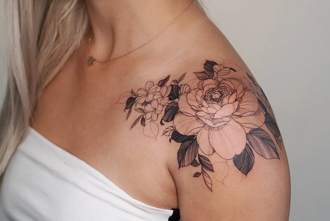 A floral tattoo with large peonies, smaller flowers, and leaves on a woman's shoulder and upper arm.