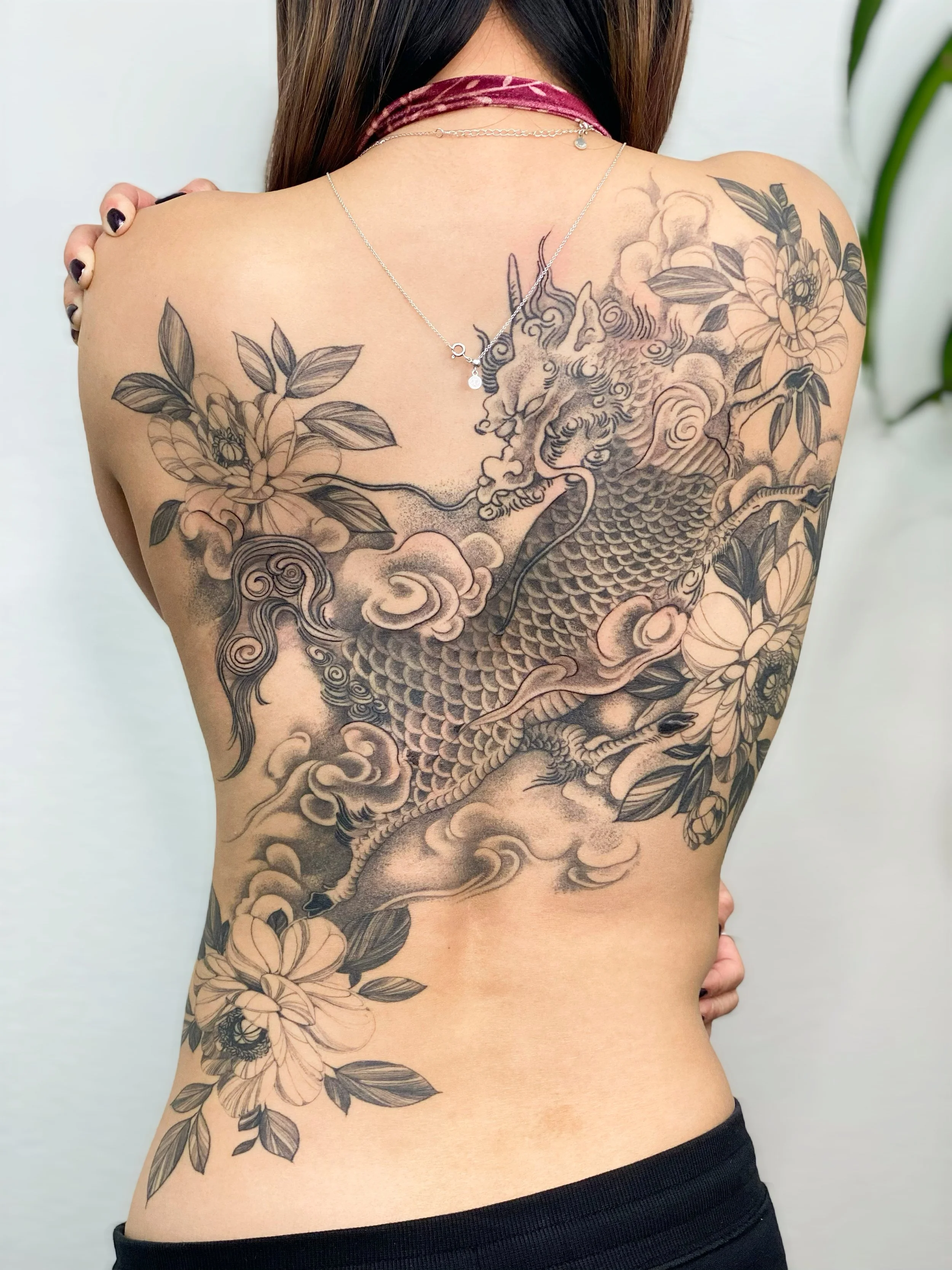 Back tattoo of a dragon with floral elements on a person's back.