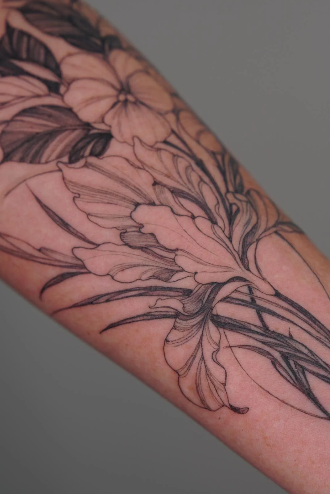 Close-up of a person's arm with a floral tattoo in black ink, featuring detailed flowers and leaves.