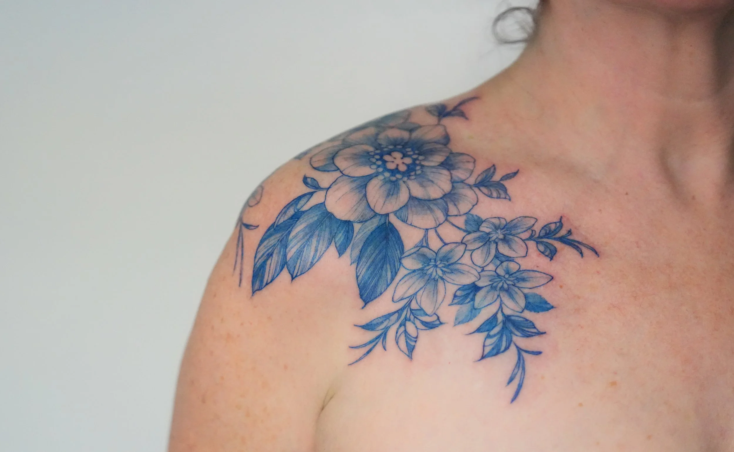 A close-up of a person's shoulder and collarbone with a large blue floral tattoo.