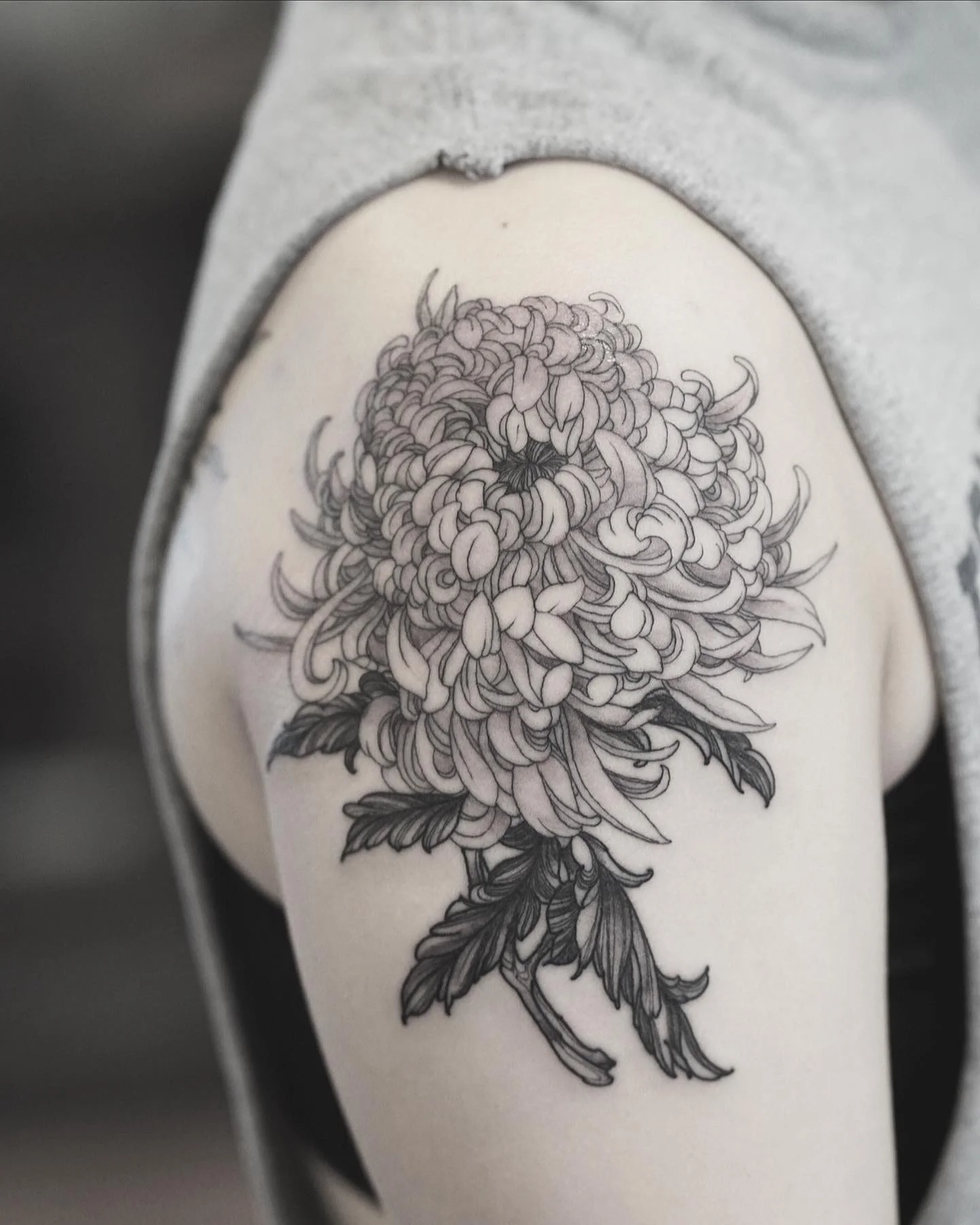 Line art tattoo of a detailed flower with many petals and leaves on a person's leg.