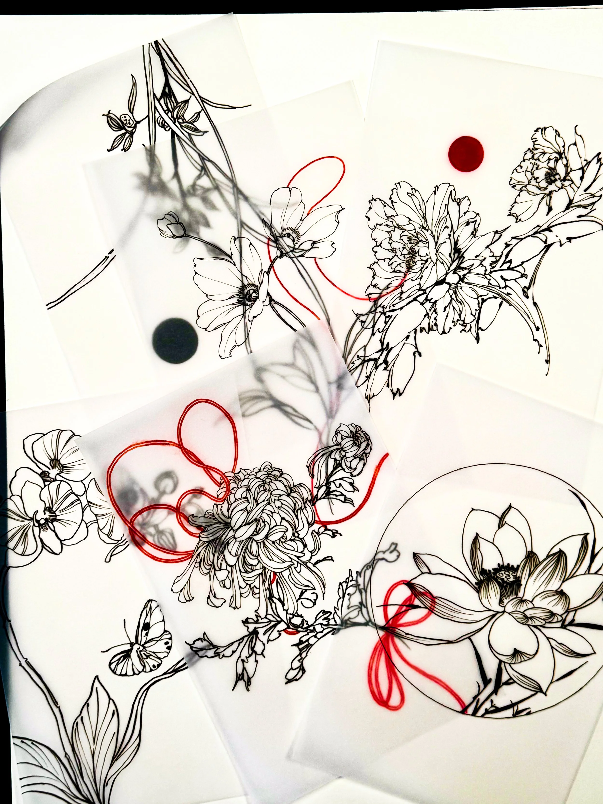 Outline floral drawings on white paper, some with red and black thread accents and black or red dots, layered on a white surface.