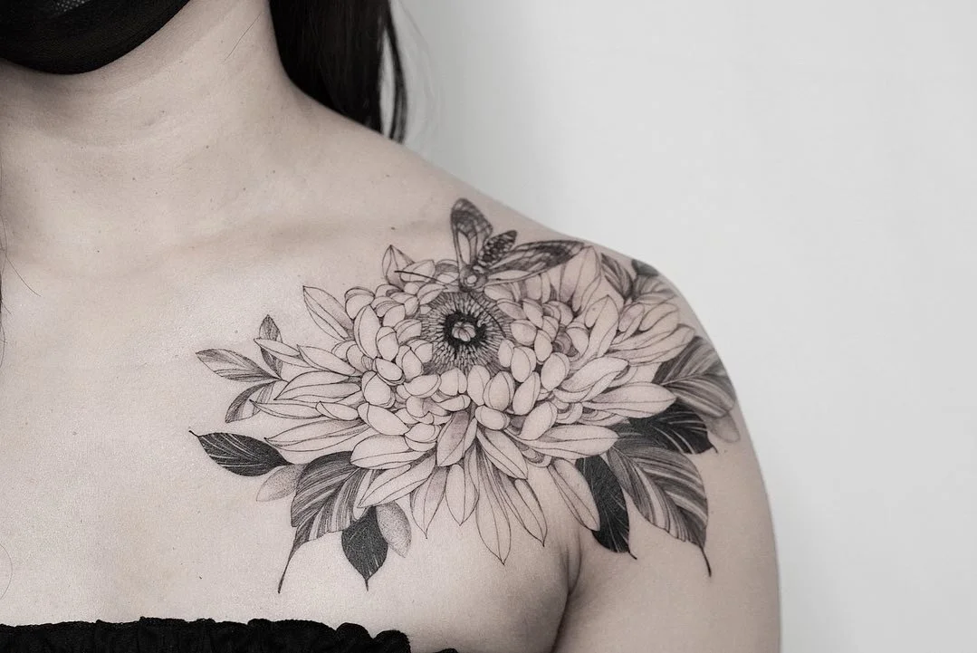 Detailed black and gray tattoo of a large flower with leaves and a butterfly on the woman's shoulder.