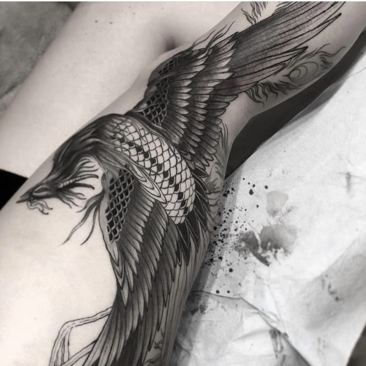 Black and gray tattoo of a dragon with detailed scales, wings, and fierce facial features on a person's arm.