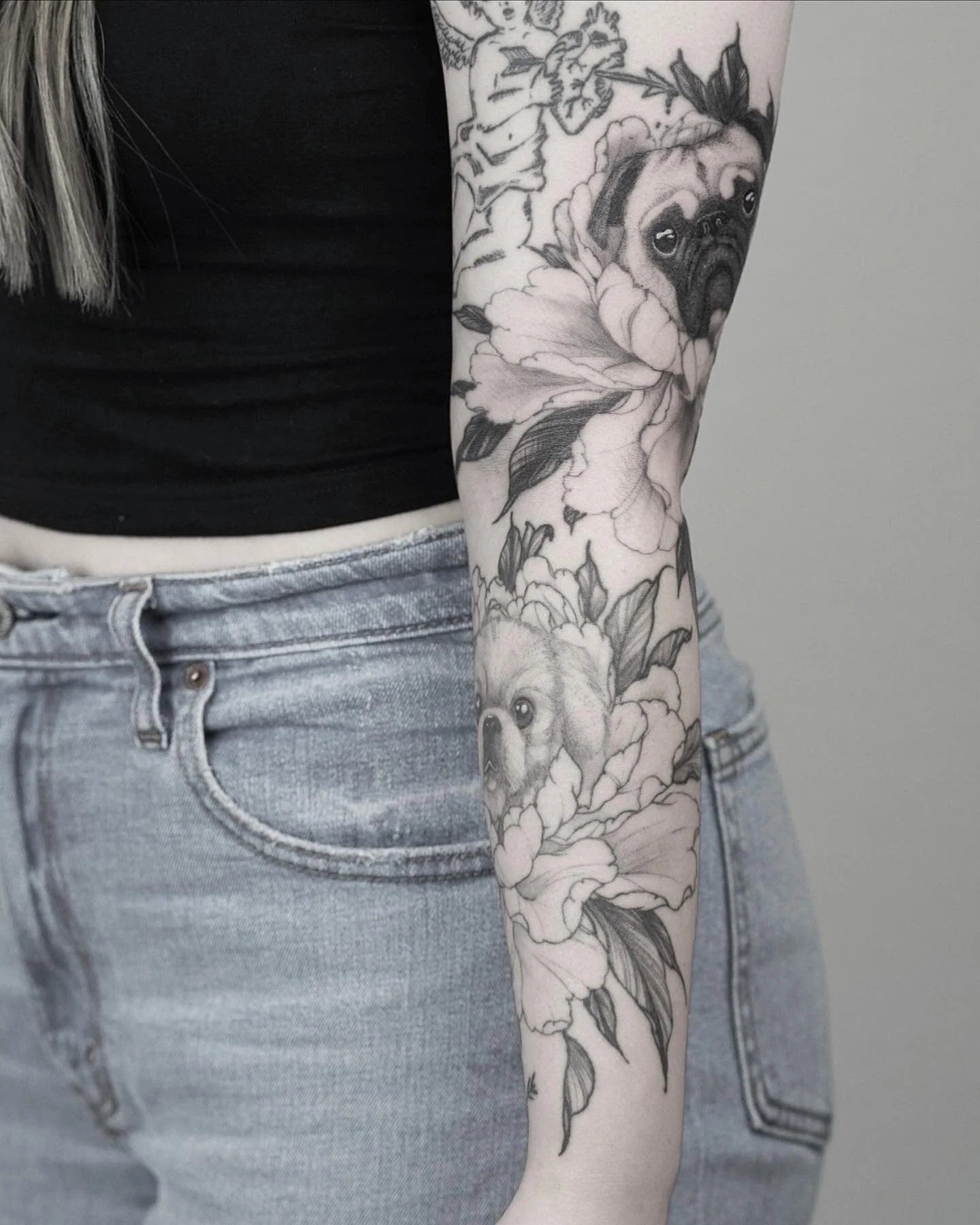 Black and gray tattoo of a pug and a small dog surrounded by large flowers on a person's arm.