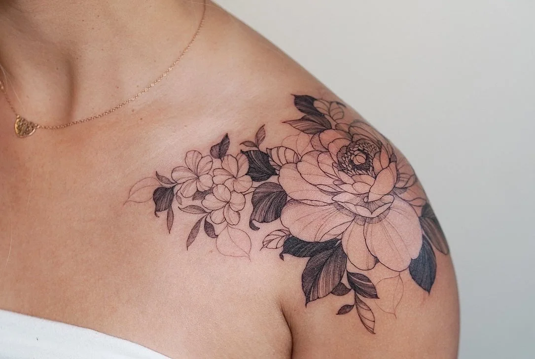 A floral tattoo with black outlines of flowers and leaves on a person's shoulder and upper arm.