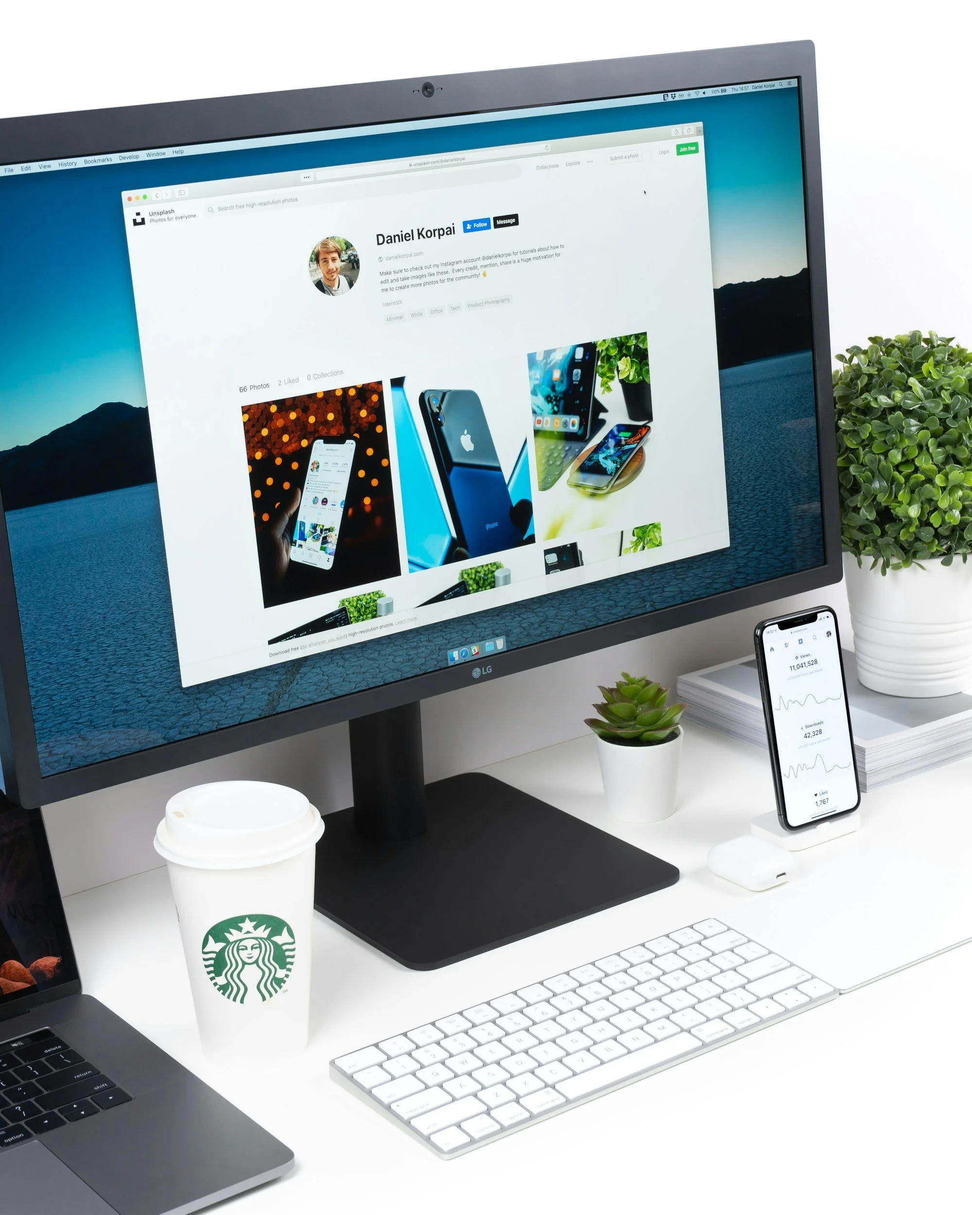 Computer monitor displaying a webpage, smartphone on a stand showing financial data, coffee cup, small potted plants, keyboard, laptop, and notebook on a white desk.