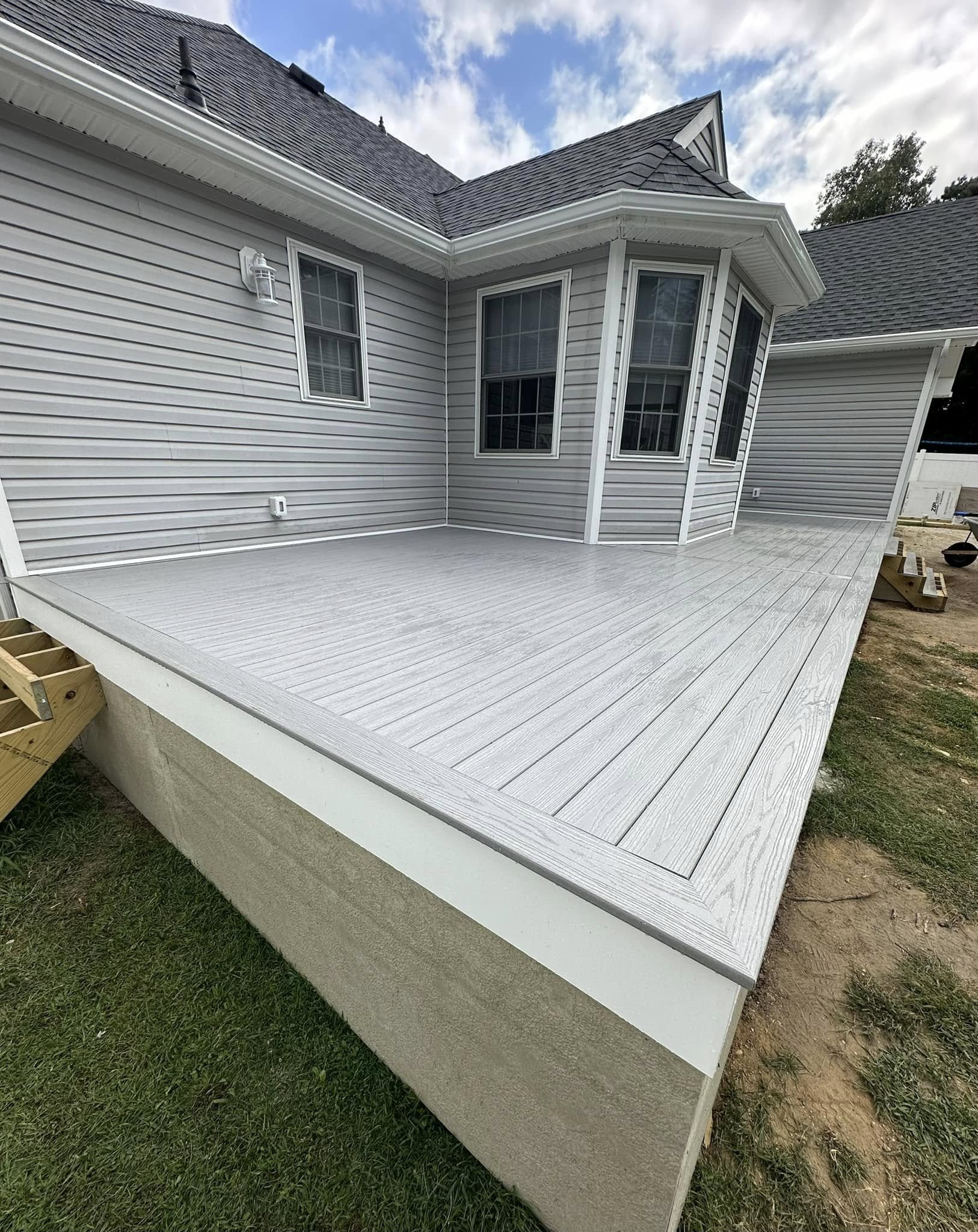 Exterior view of a house with gray siding and a new gray deck, under a partly cloudy sky.