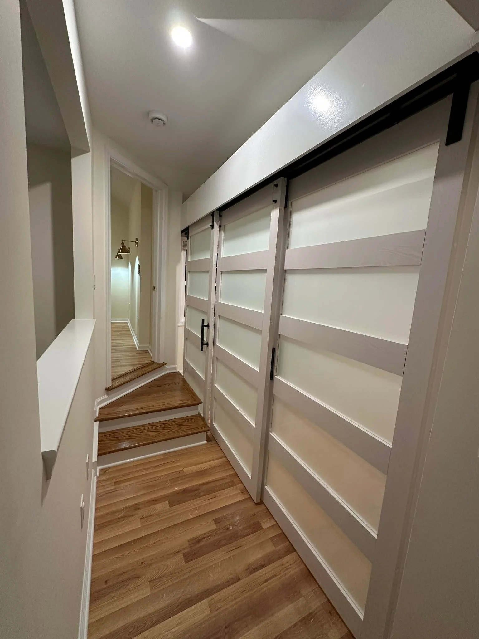 Hallway with wooden stairs, white walls, and sliding barn doors with frosted glass panels.