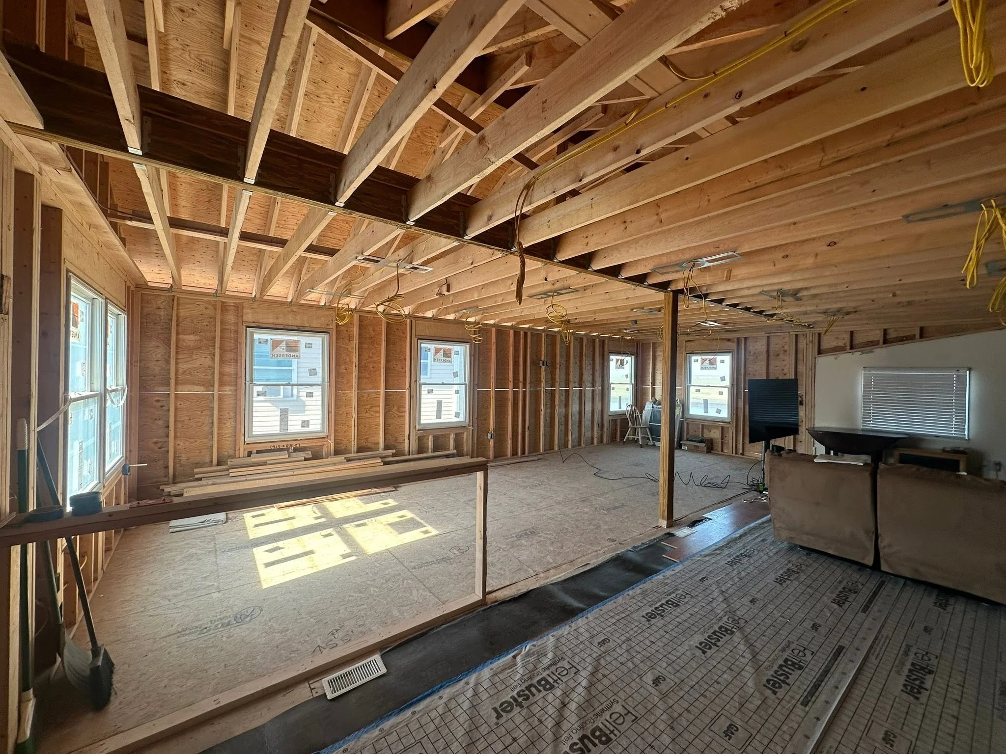 Interior of a house under construction with exposed wooden framing, electrical wiring, and large windows.