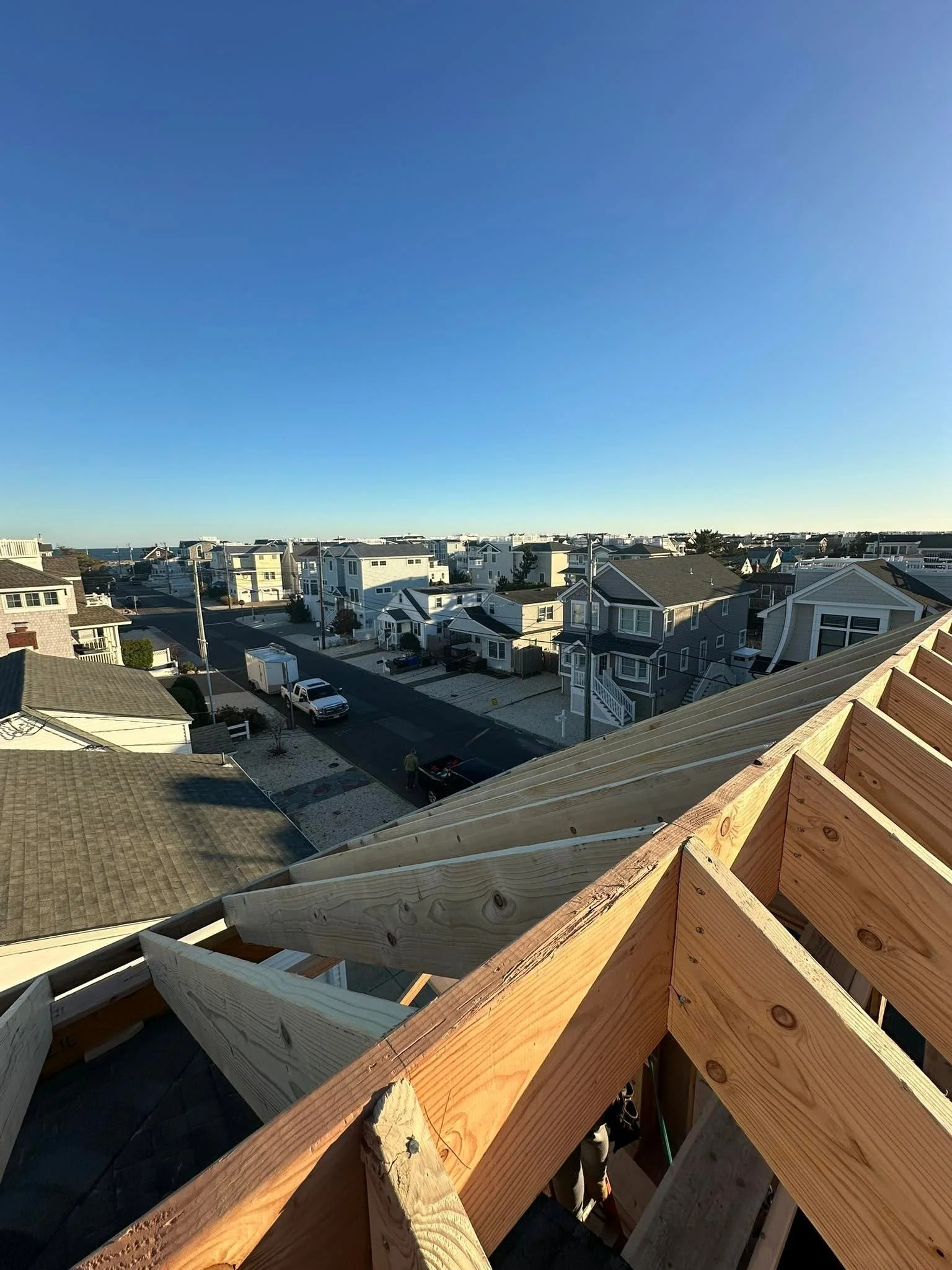A view from a building under construction overlooking a neighborhood of houses in a coastal area, with clear blue skies.