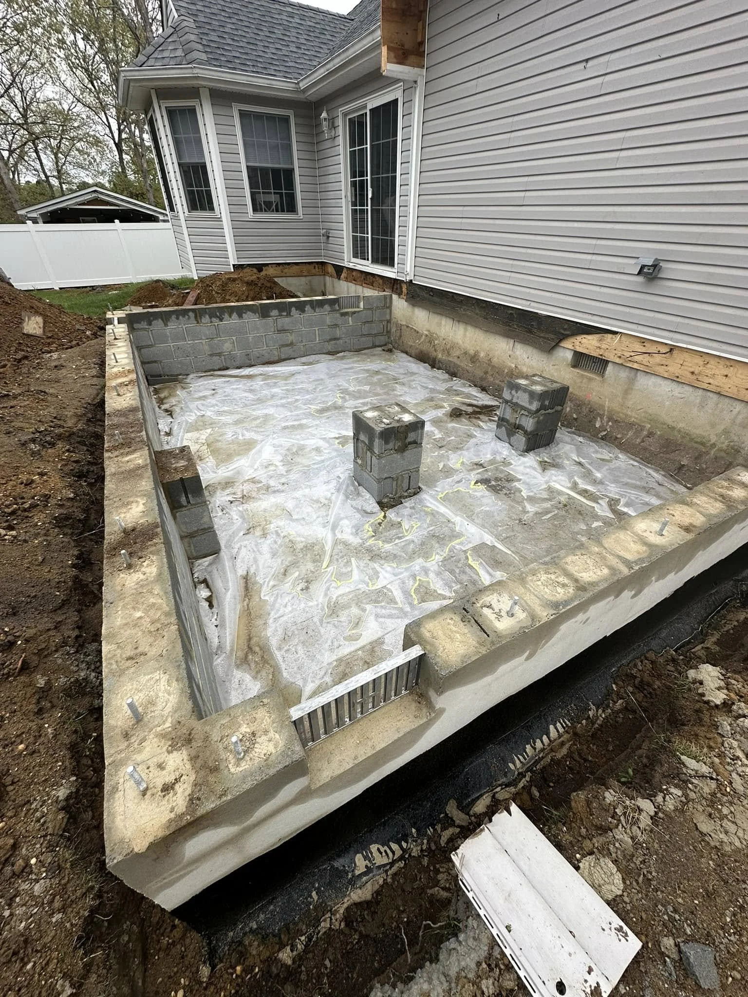 Backyard foundation of a house under construction with concrete blocks, some dirt, and construction materials visible.