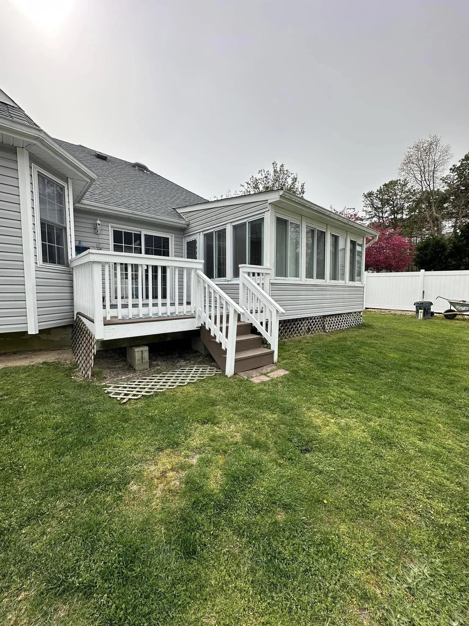 A house with grey siding, a white porch with stairs, and a sunlit backyard with green grass and trees.