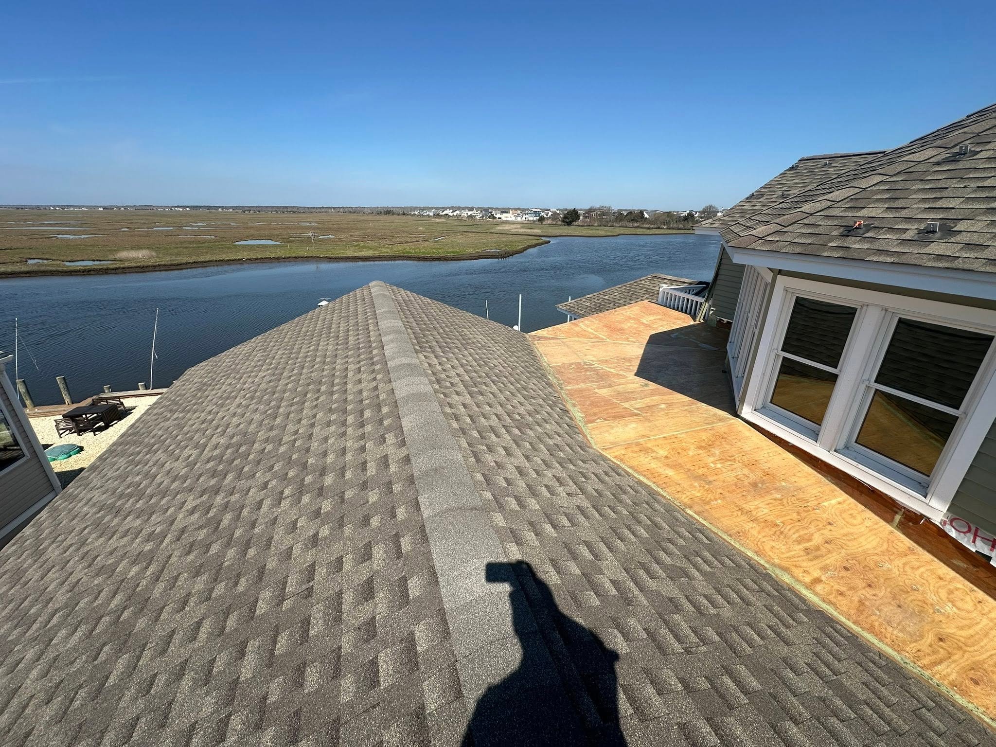 View from a house overlooking a river with marshland and houses in the distance, under a clear blue sky.