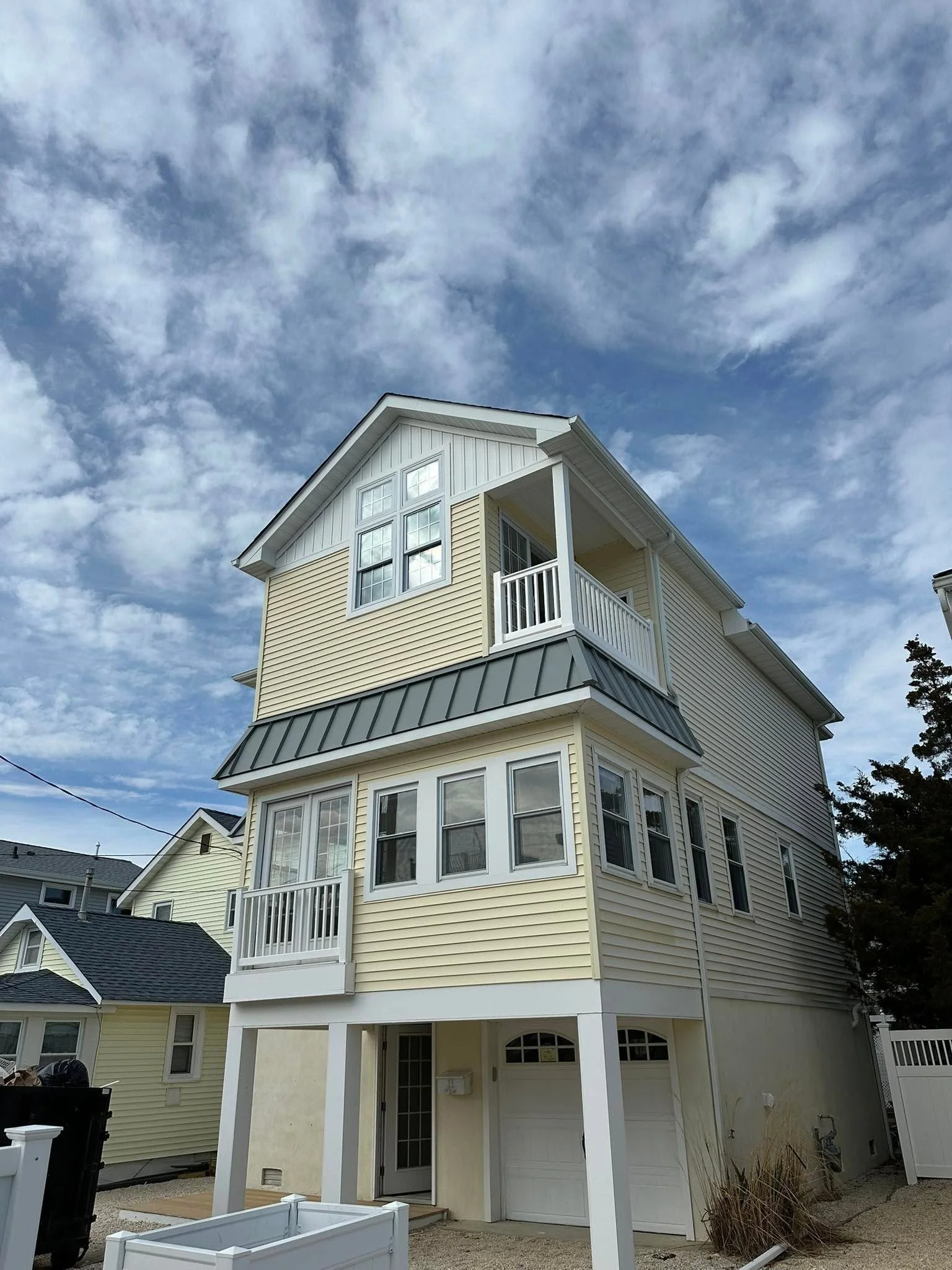 A multi-story yellow house with white trim, a small balcony, and a garage, under a partly cloudy sky.