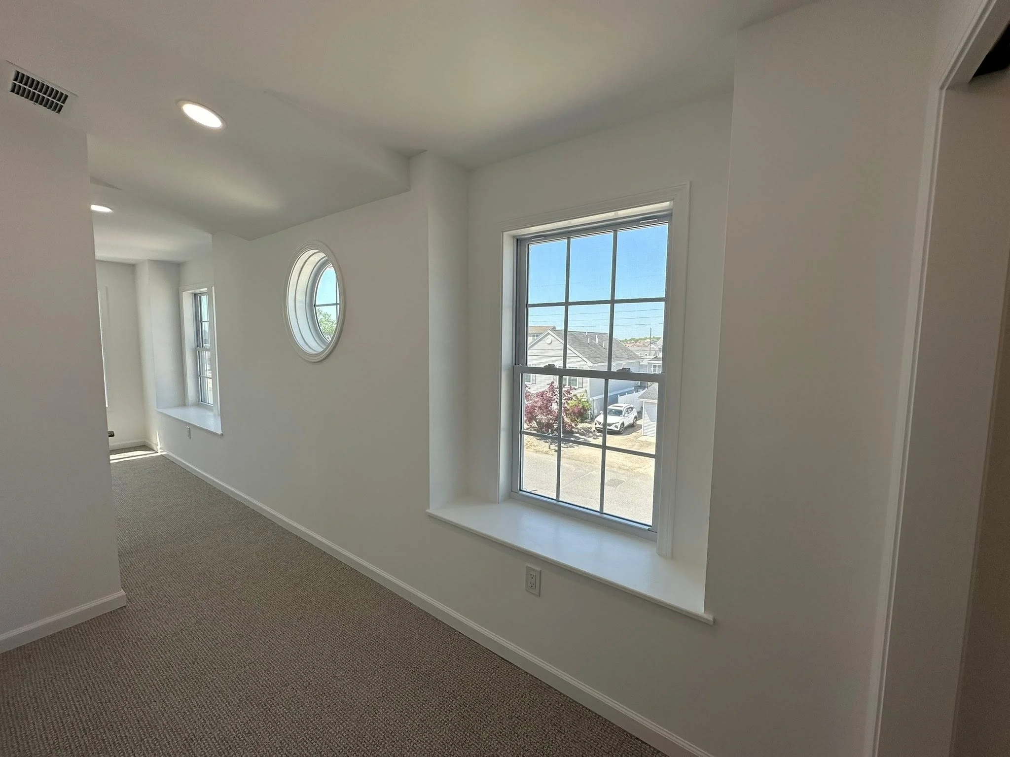 Interior of a modern house with white walls, large windows, and a tan carpet.