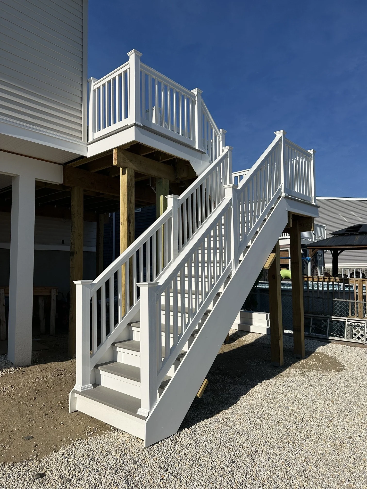 White wooden staircase and porch railing under construction next to a house with vinyl siding, with blue sky in the background.