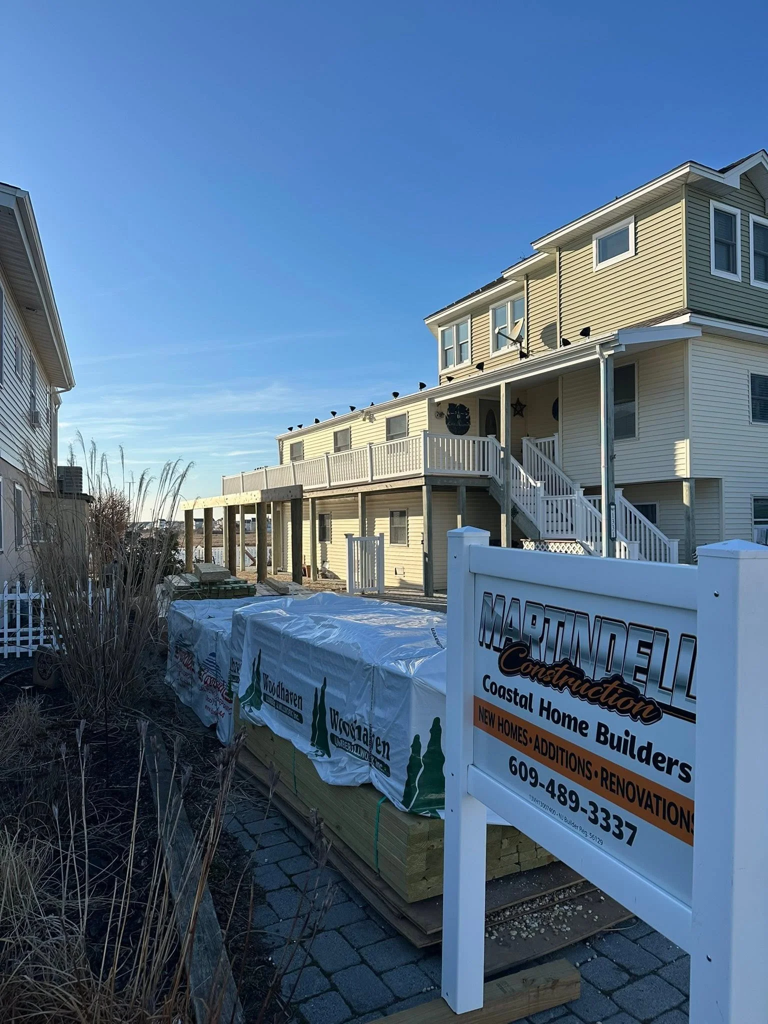 Construction site with new yellow house being built, with piles of materials and construction sign in the foreground.