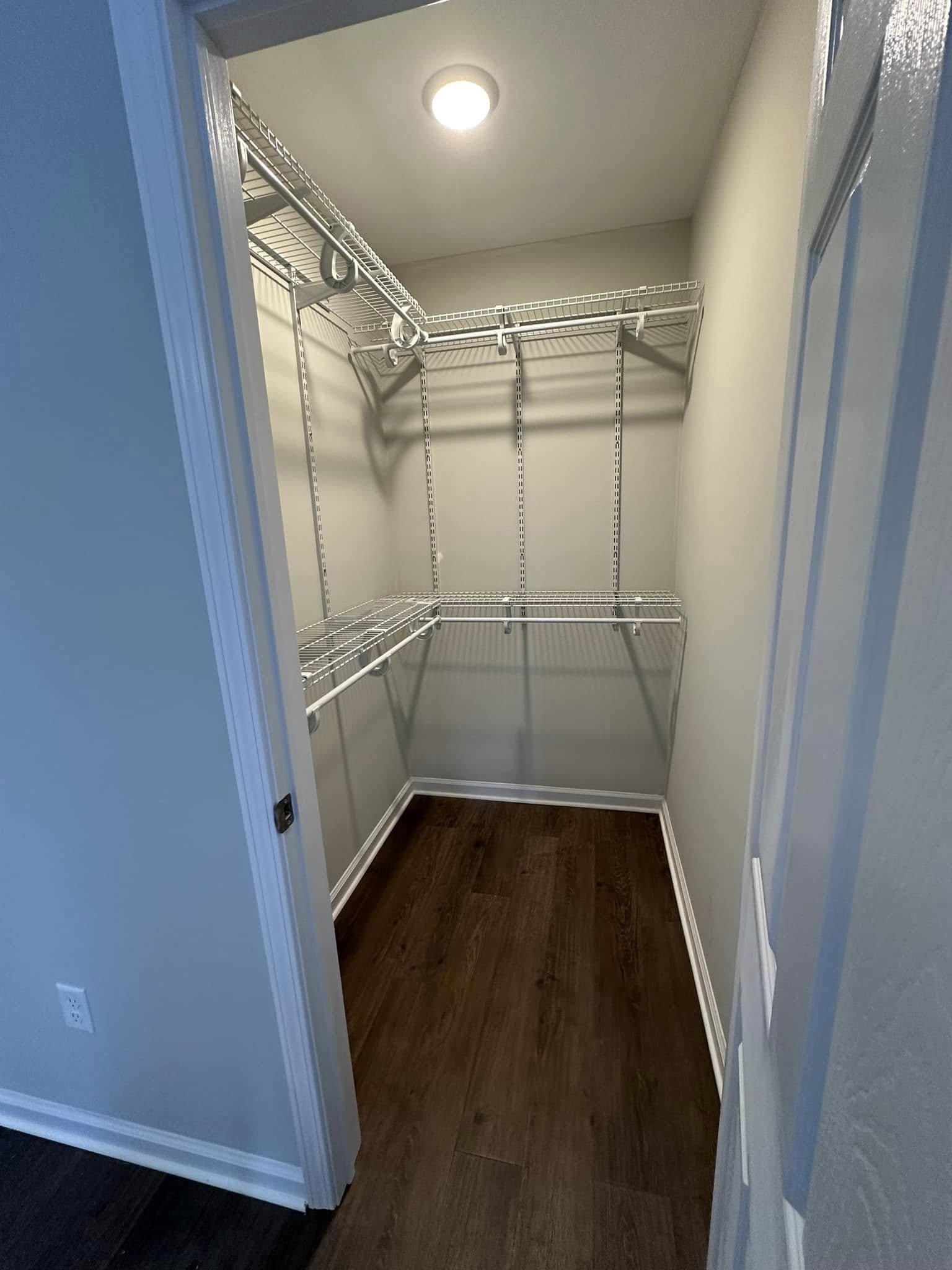 Empty walk-in closet with wire shelves and a wood floor, illuminated by a ceiling light.