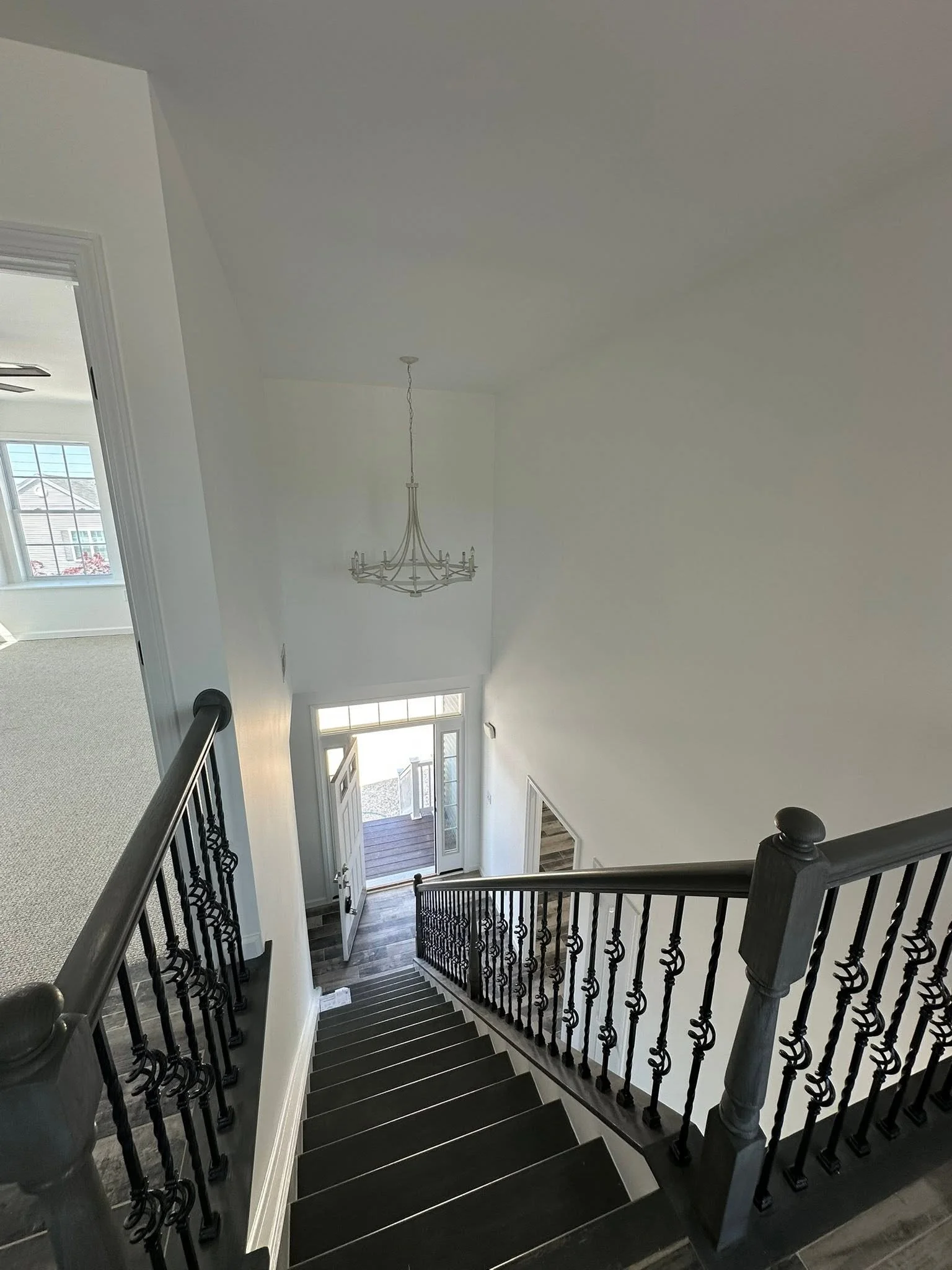 View from top of staircase looking downward, showing black steps with white edge stripes, black wrought iron railing, front door with glass panels, and porch area with a wooden deck outside.