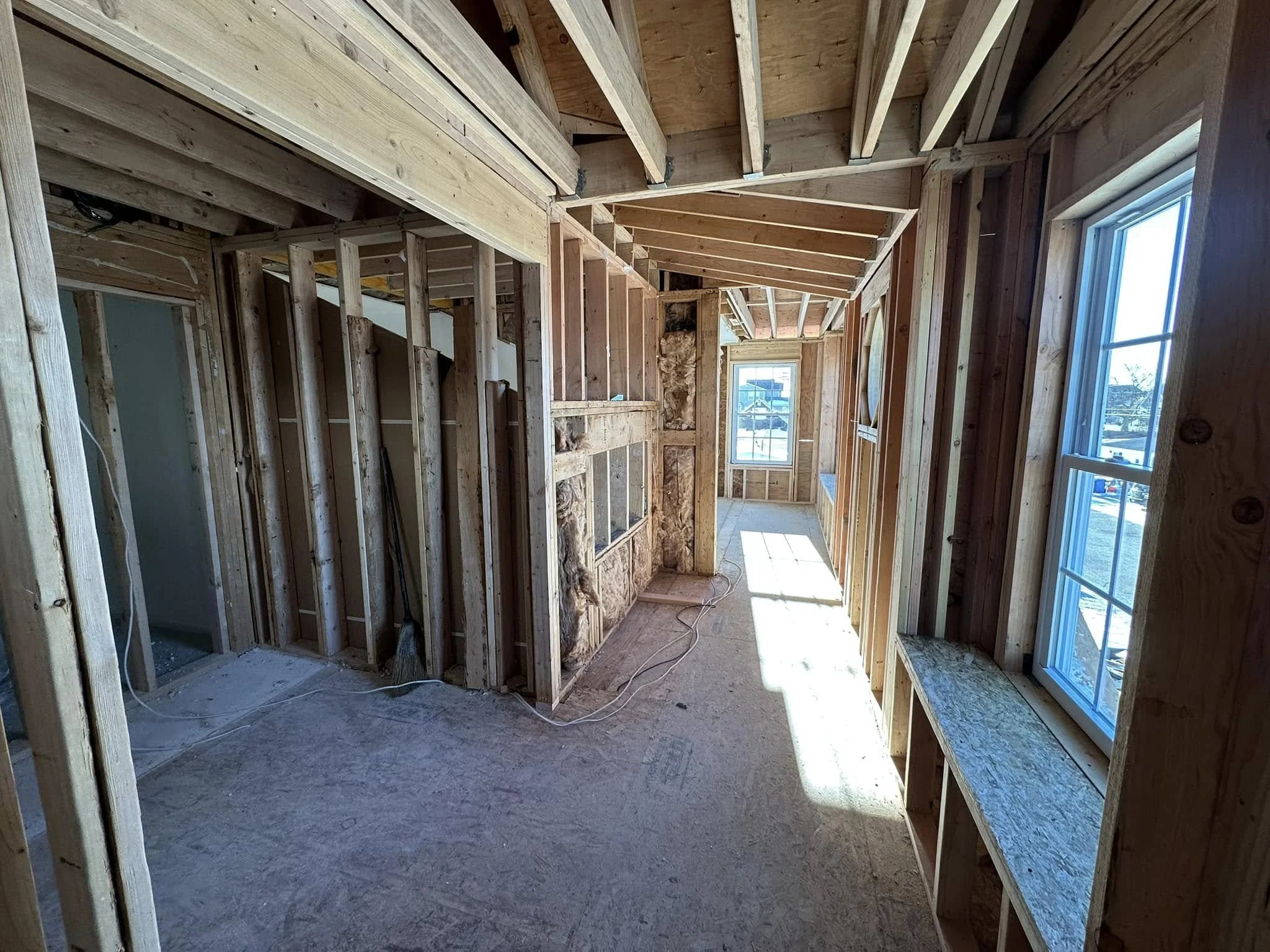 Interior view of a house under construction with exposed wooden framing and large windows.