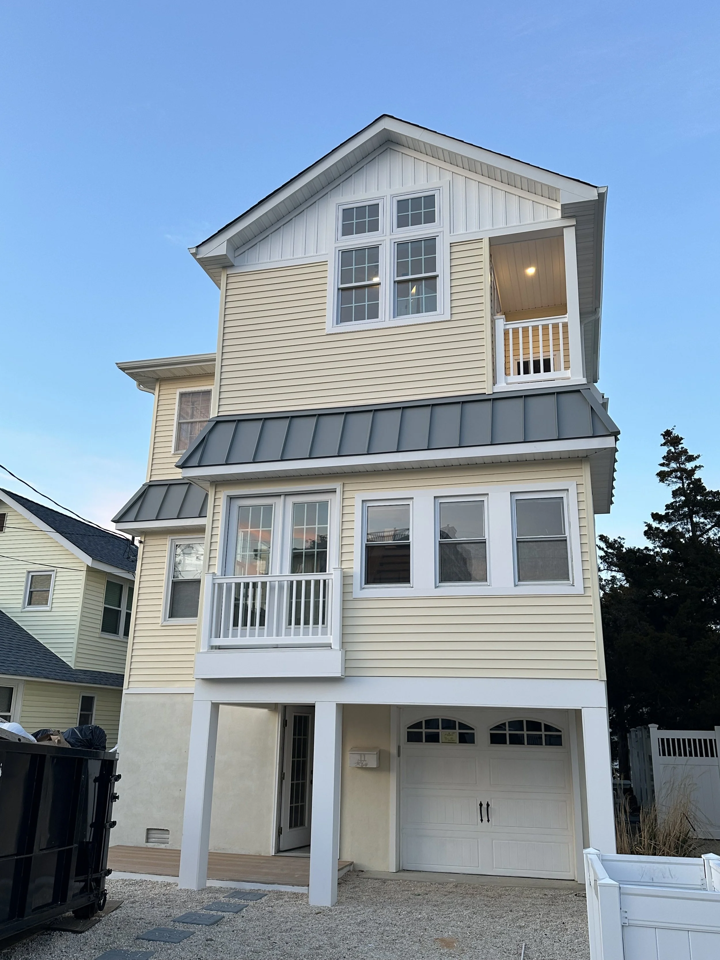 A tall, three-story house with beige siding, white trim, multiple windows, and a garage on the ground level.