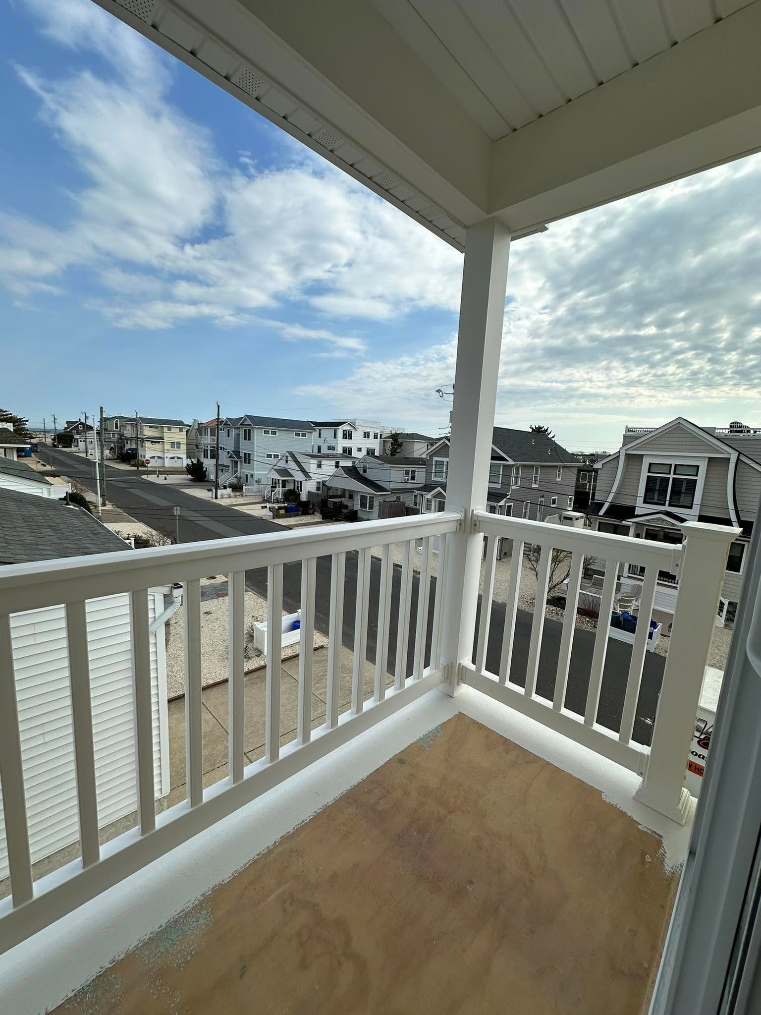 View from a balcony showing a neighborhood with multi-story houses, utility poles, and a partly cloudy sky.