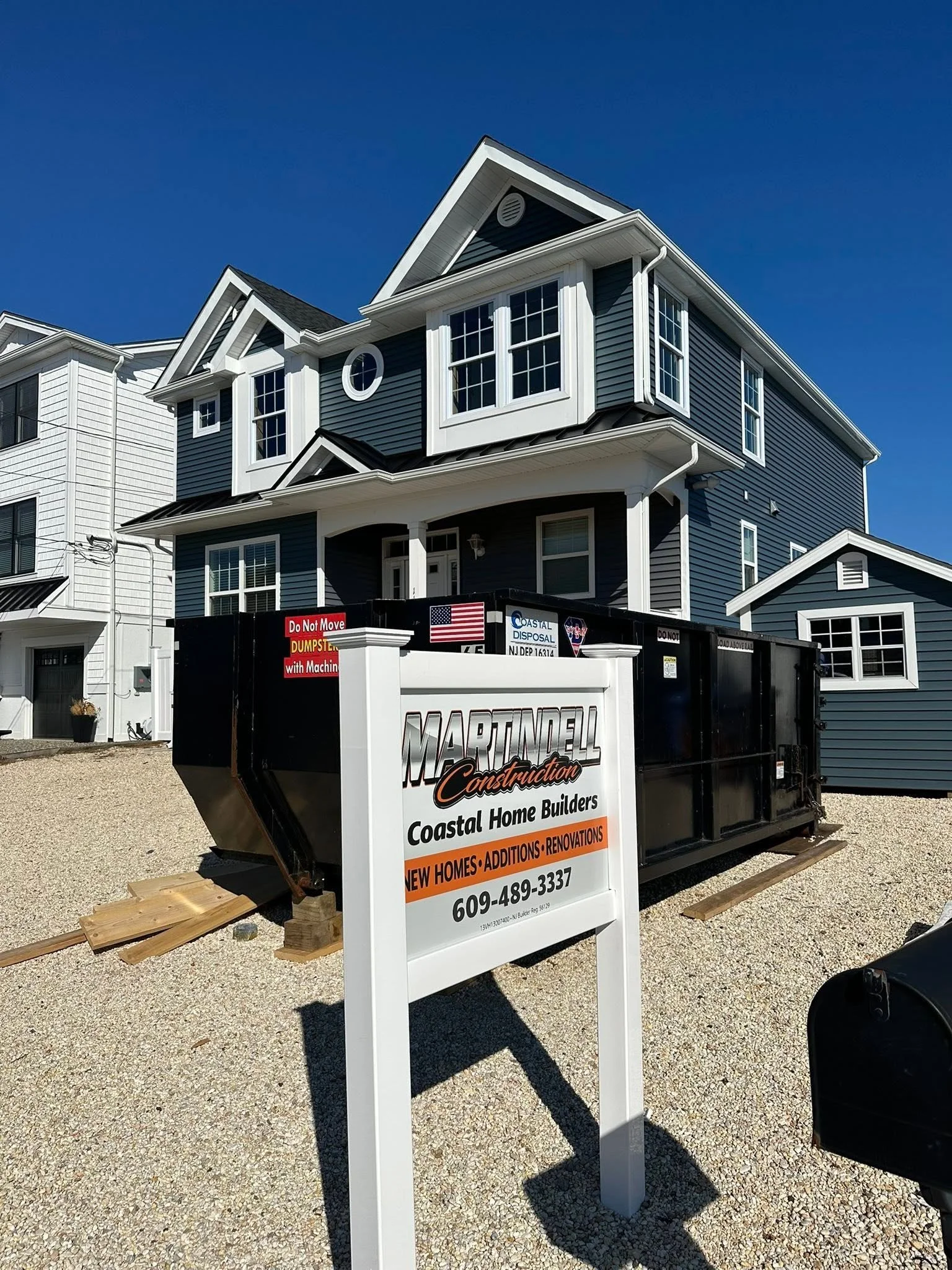 Signboard for Martindell Construction advertising new homes, additions, and renovations, with a phone number, placed in front of a house with blue siding and white trim under a clear blue sky.