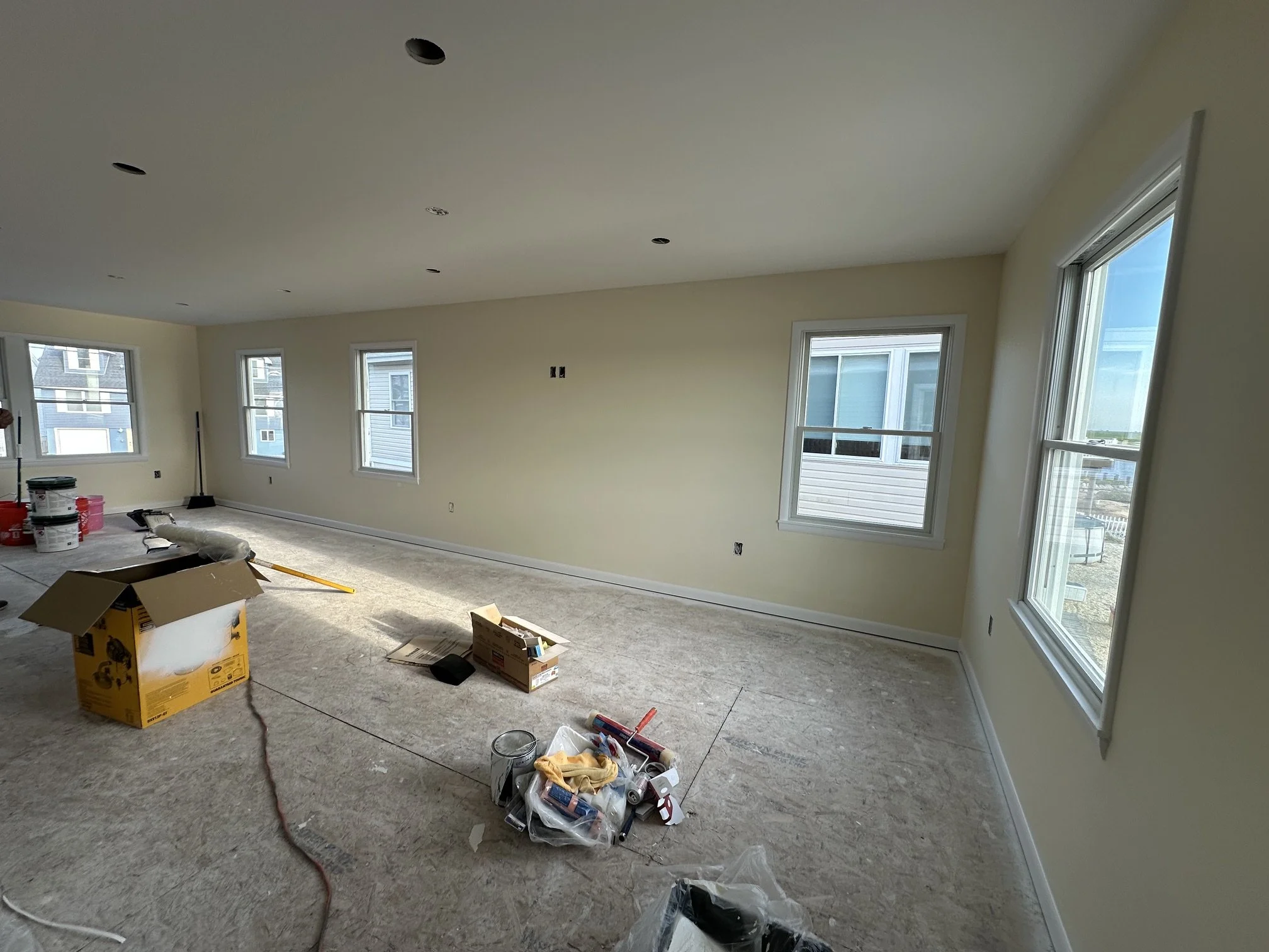 Interior of a room under renovation with multiple windows, construction supplies, and tools scattered on the floor.