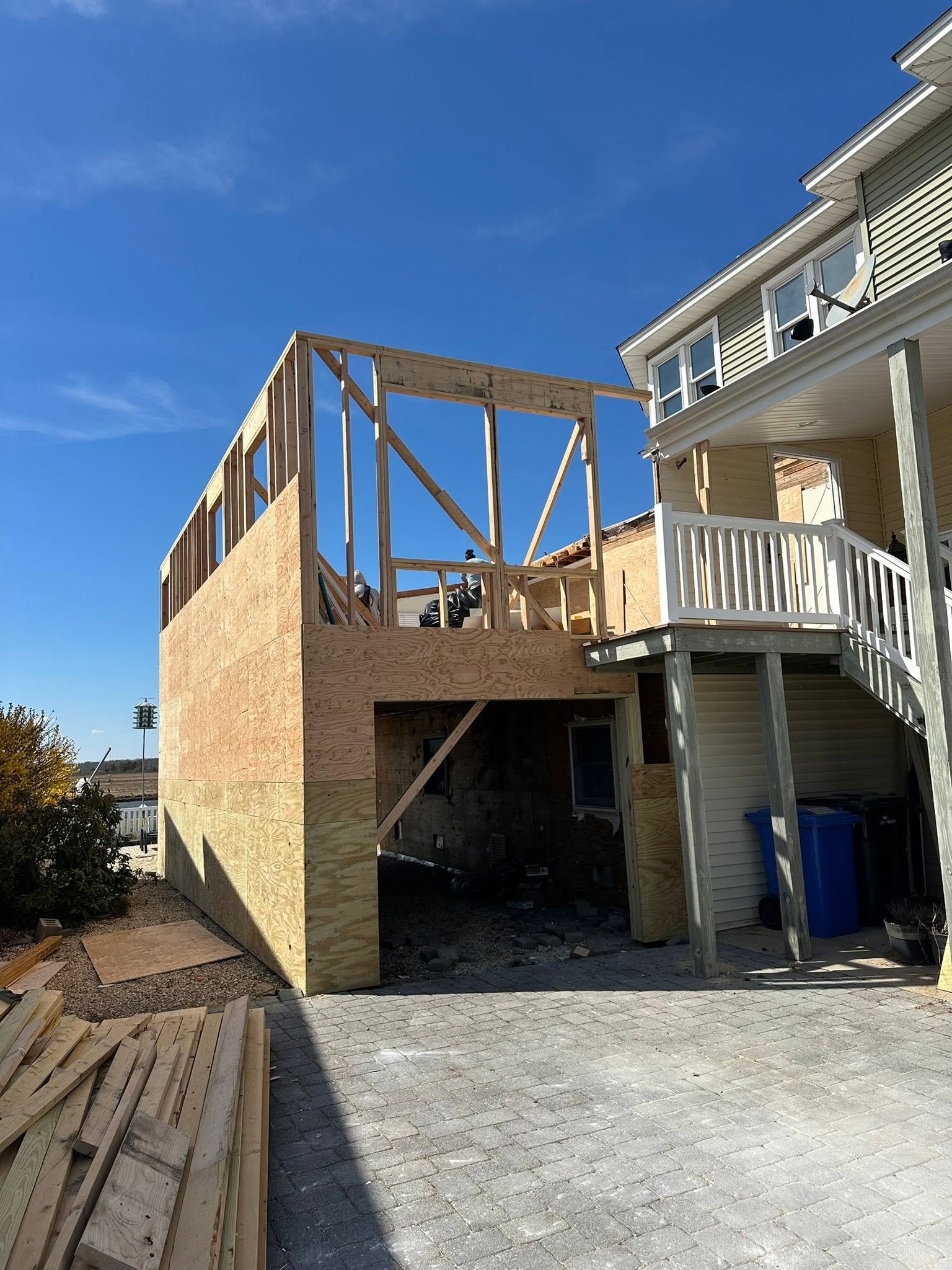 House under construction with wooden framing and scaffolding, blue sky, and brick driveway.