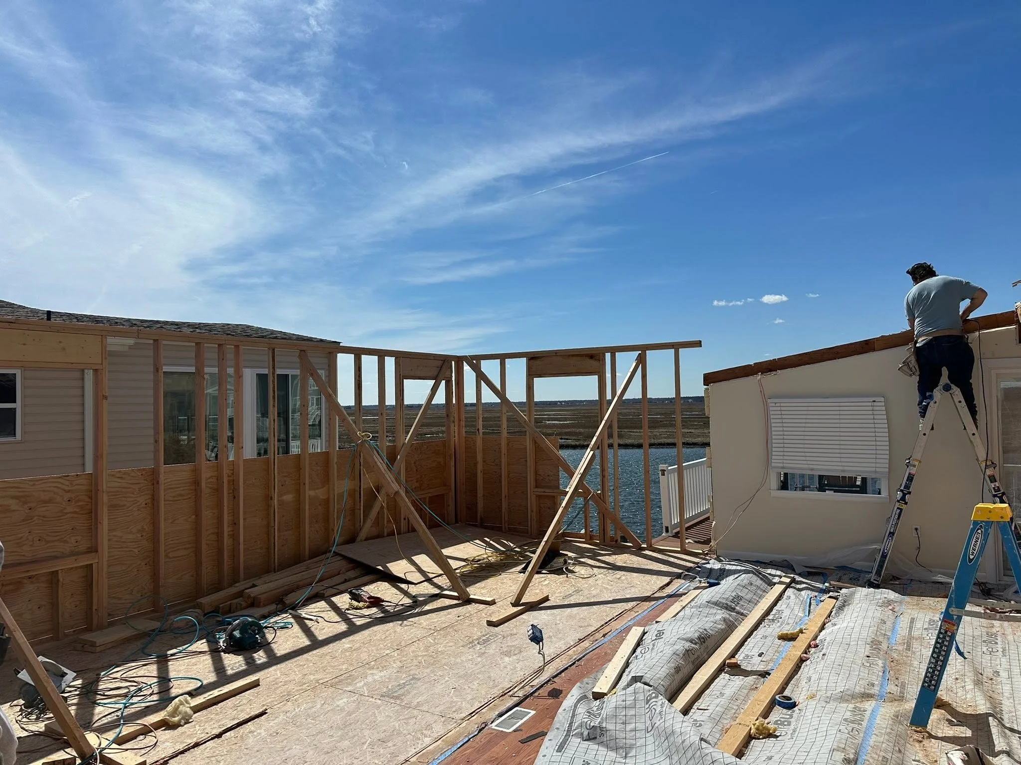 Construction site with a workers building a house outdoors. Partially built wooden framing, tools, and construction materials visible.