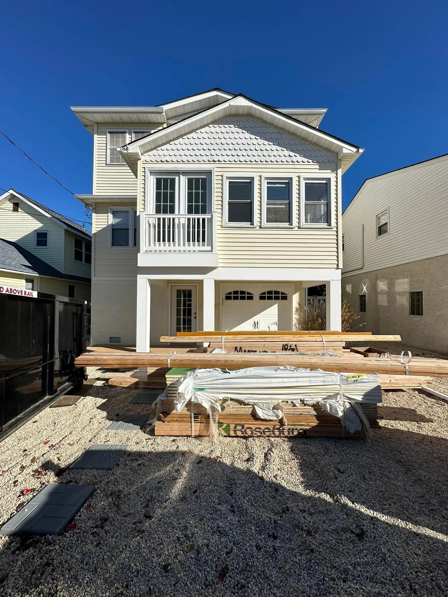 Front of a two-story house under construction, with building materials and gravel in the yard.