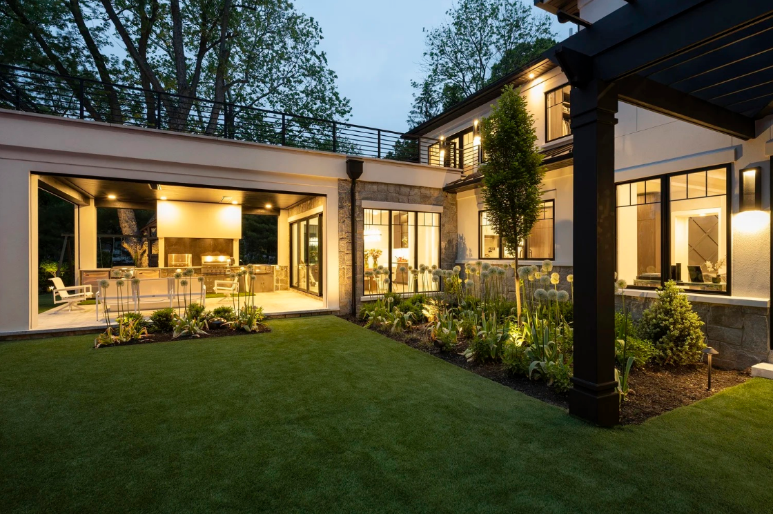 An outdoor space lit at night. Contains a well-maintained garden and outdoor kitchen space